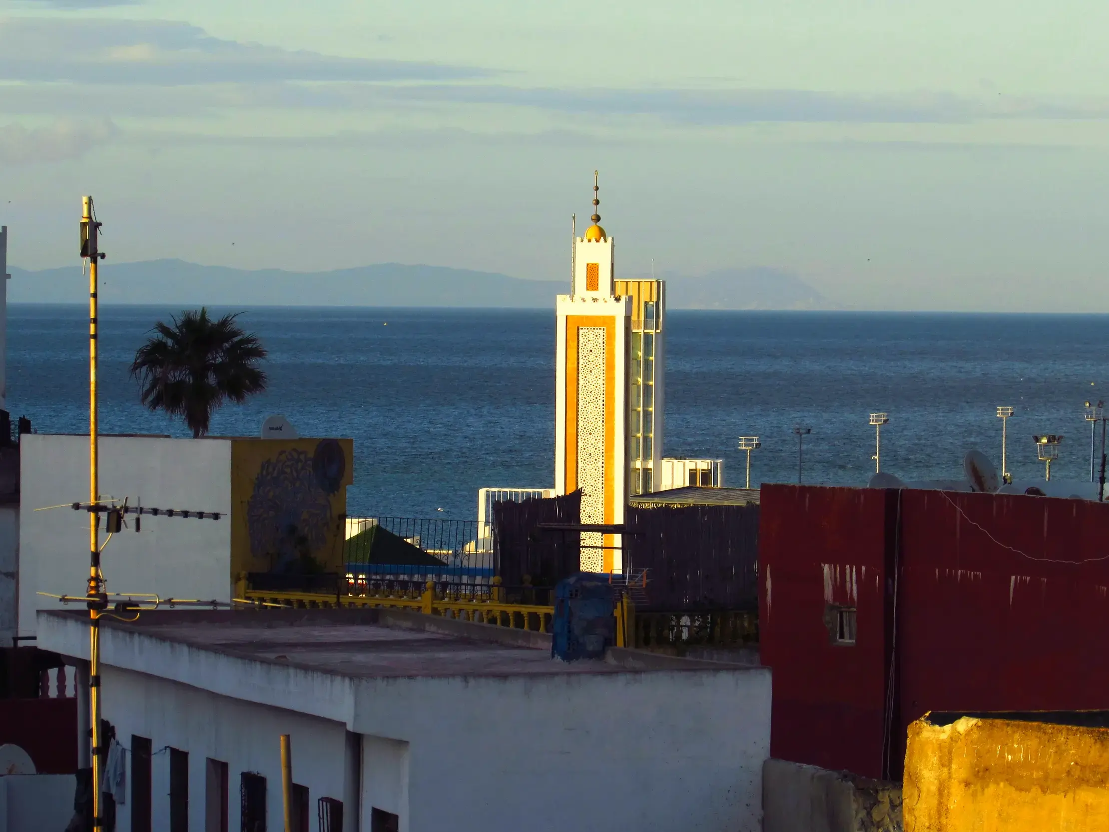 Blick von einem Riad über die Dächer von Tanger mit einem gelben Minarett auf die Straße von Gibraltar und Spanien.