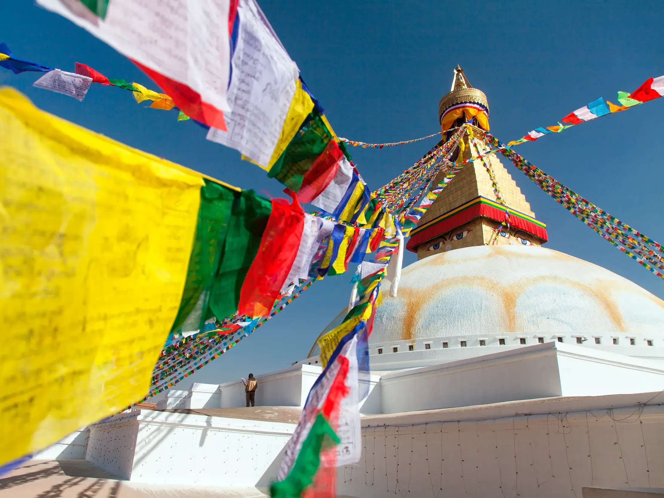 Bunte Gebetsfahnen wehen im Wind vor dem weißen Kuppelbau des buddhistischen Stupa von Bodnath in Kathmandu, Nepal.
