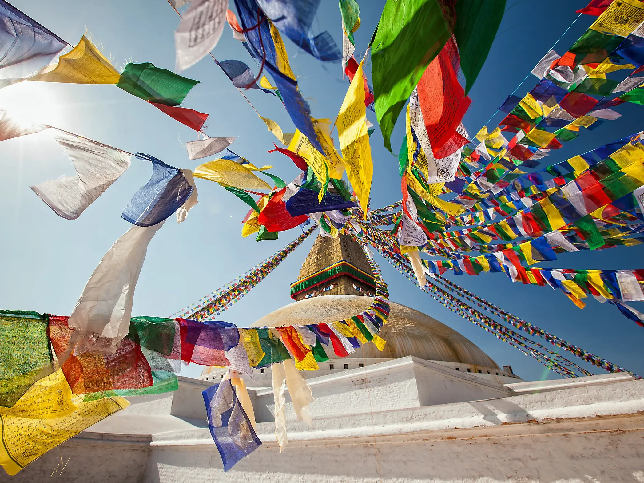 Bunte Gebetsfahnen flattern im Sonnenlicht über der weißen Kuppel des Bodnath Stupa in Kathmandu, Nepal.