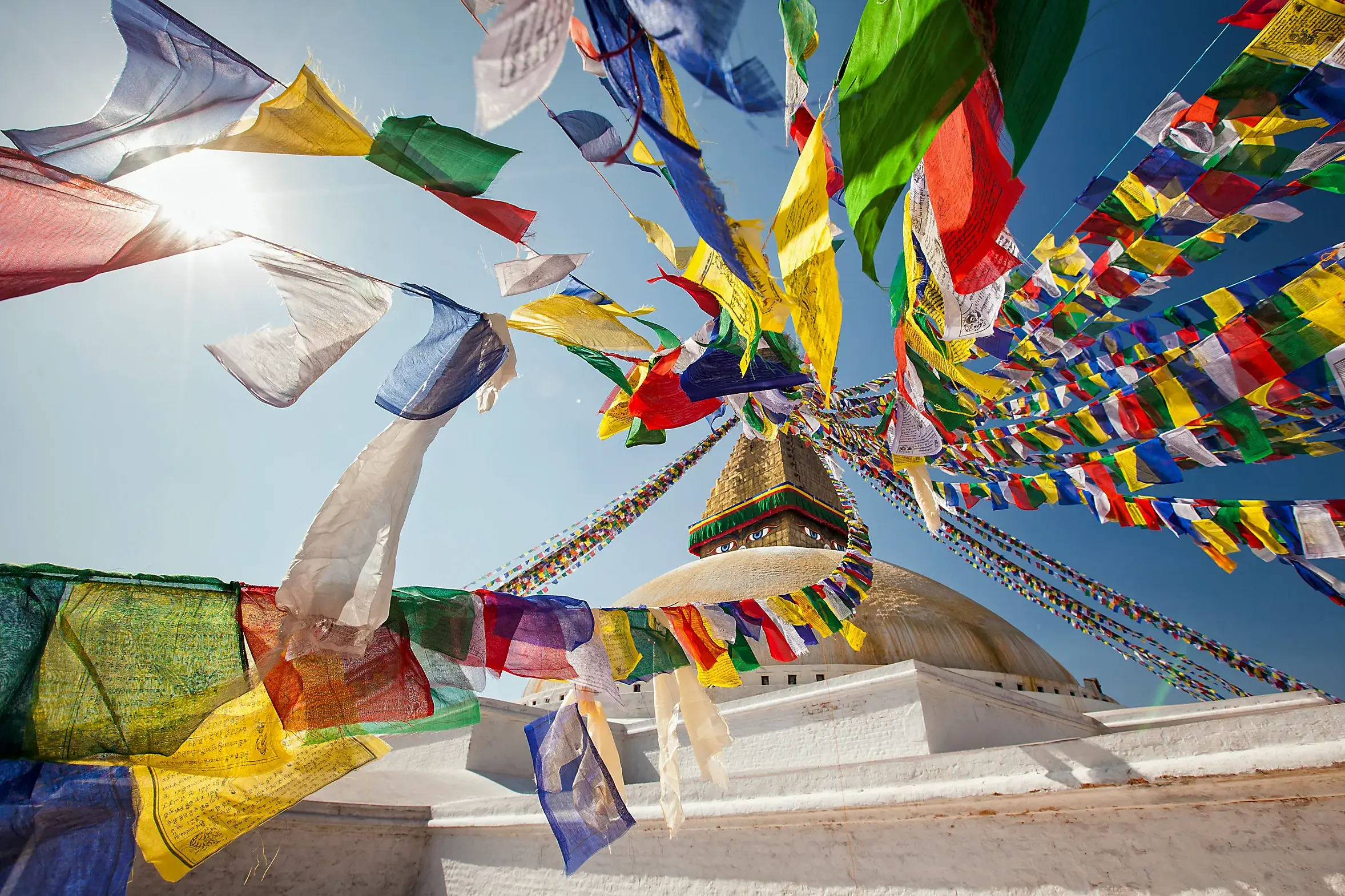 Bunte Gebetsfahnen flattern im Sonnenlicht über der weißen Kuppel des Bodnath Stupa in Kathmandu, Nepal.
