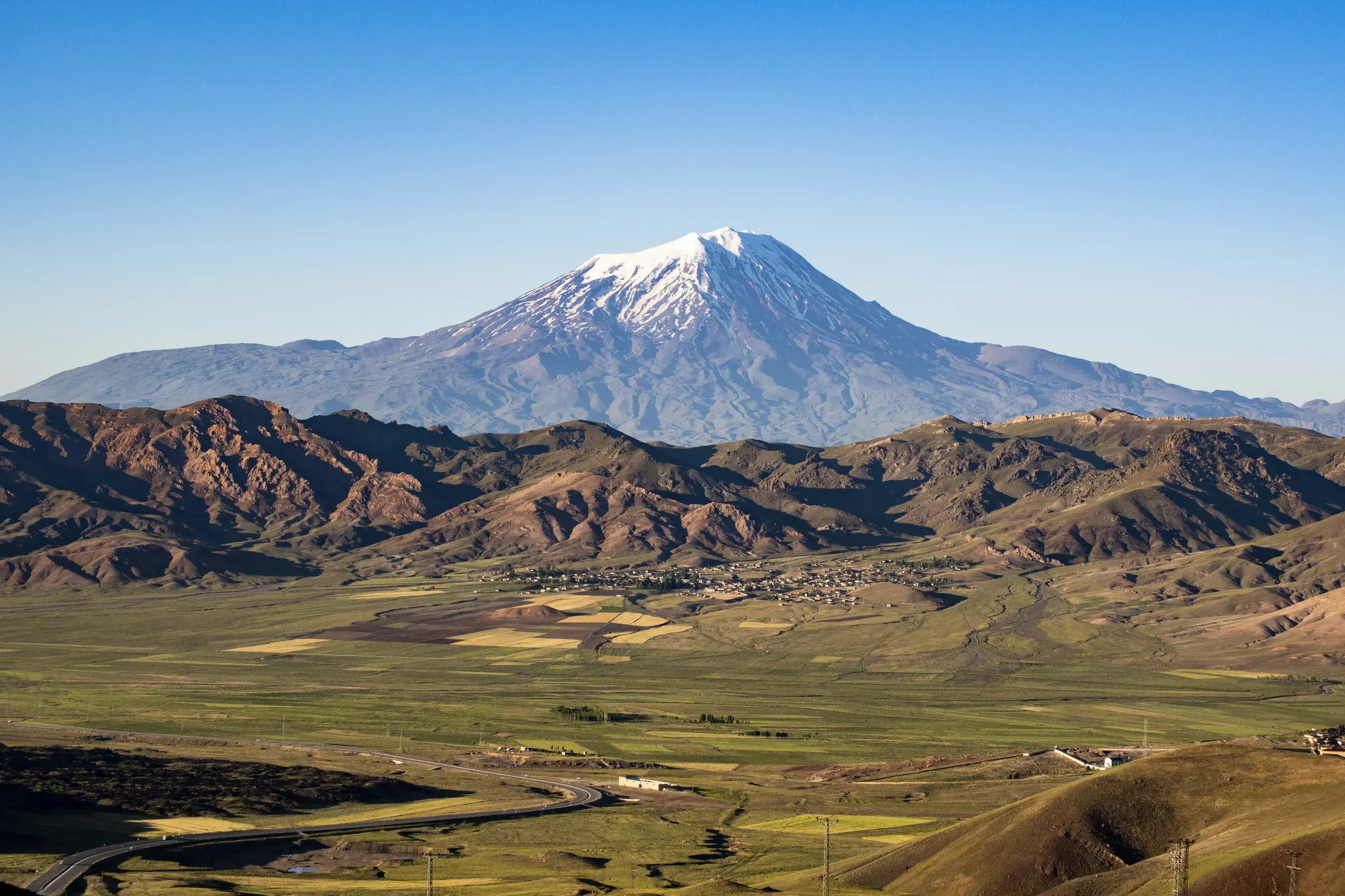 Der schneebedeckte Gipfel des Ararat ragt majestätisch über einem grünen Tal mit einer Straße nahe Doğubeyazıt auf.