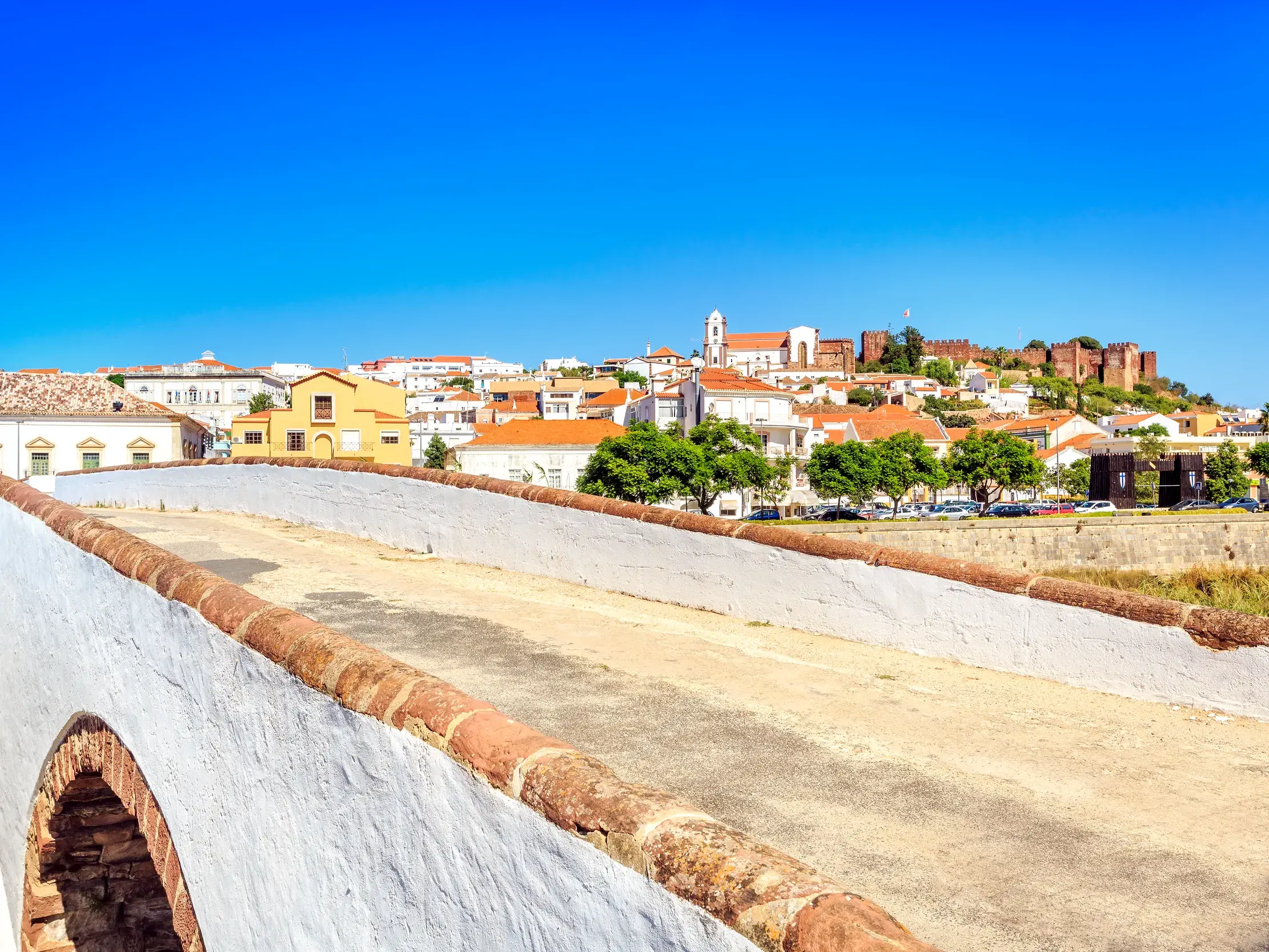 Blick von einer historischen Brücke auf die Stadt Silves mit der mächtigen Maurenburg unter blauem Himmel an der Algarve.