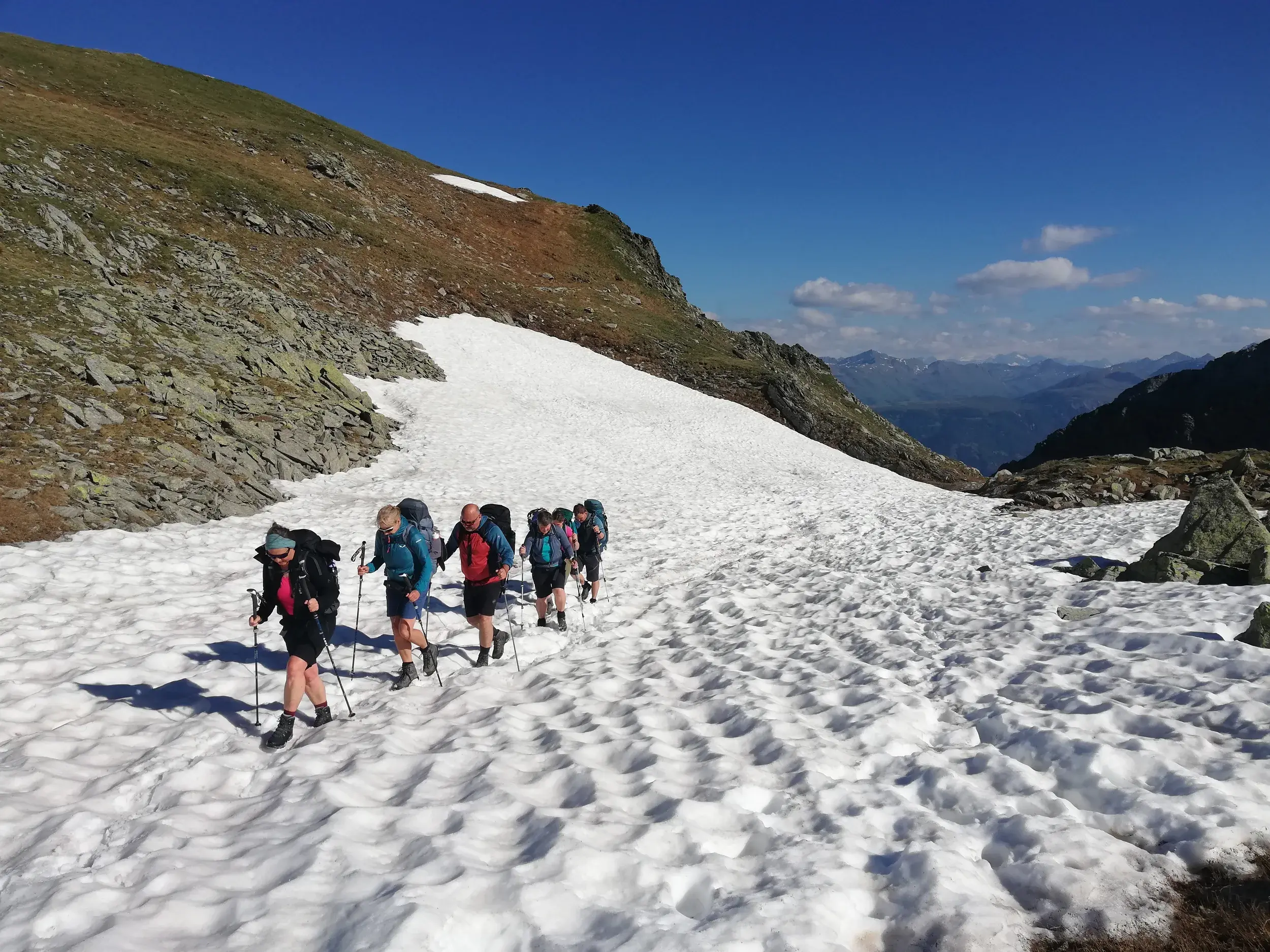 Trekking-Gruppe auf dem Karnischen Höhenweg: Wanderer queren ein Altschneefeld in der hochalpinen Bergkulisse der Alpen.