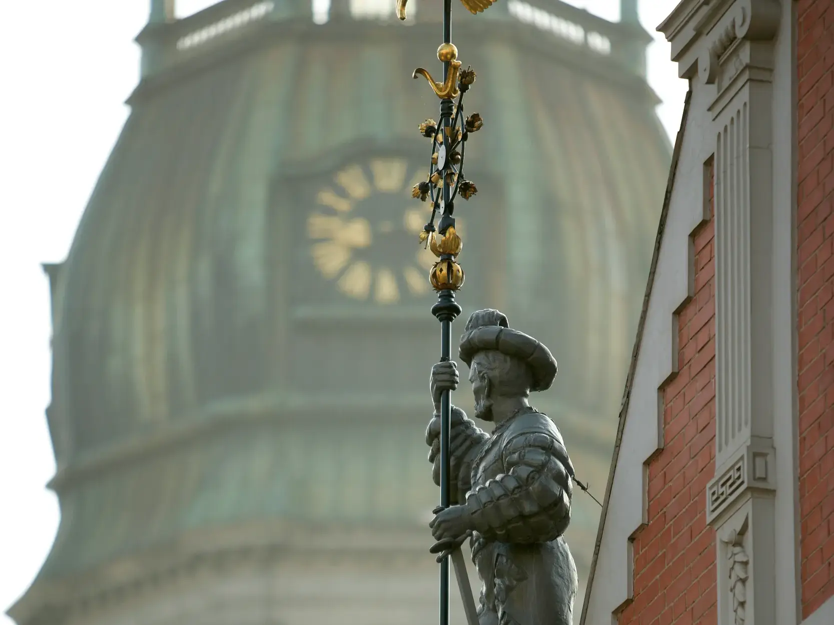 Figur am Schwarzhäupterhaus in der Altstadt von Riga mit der unscharfen Kuppel der Petrikirche im Hintergrund.