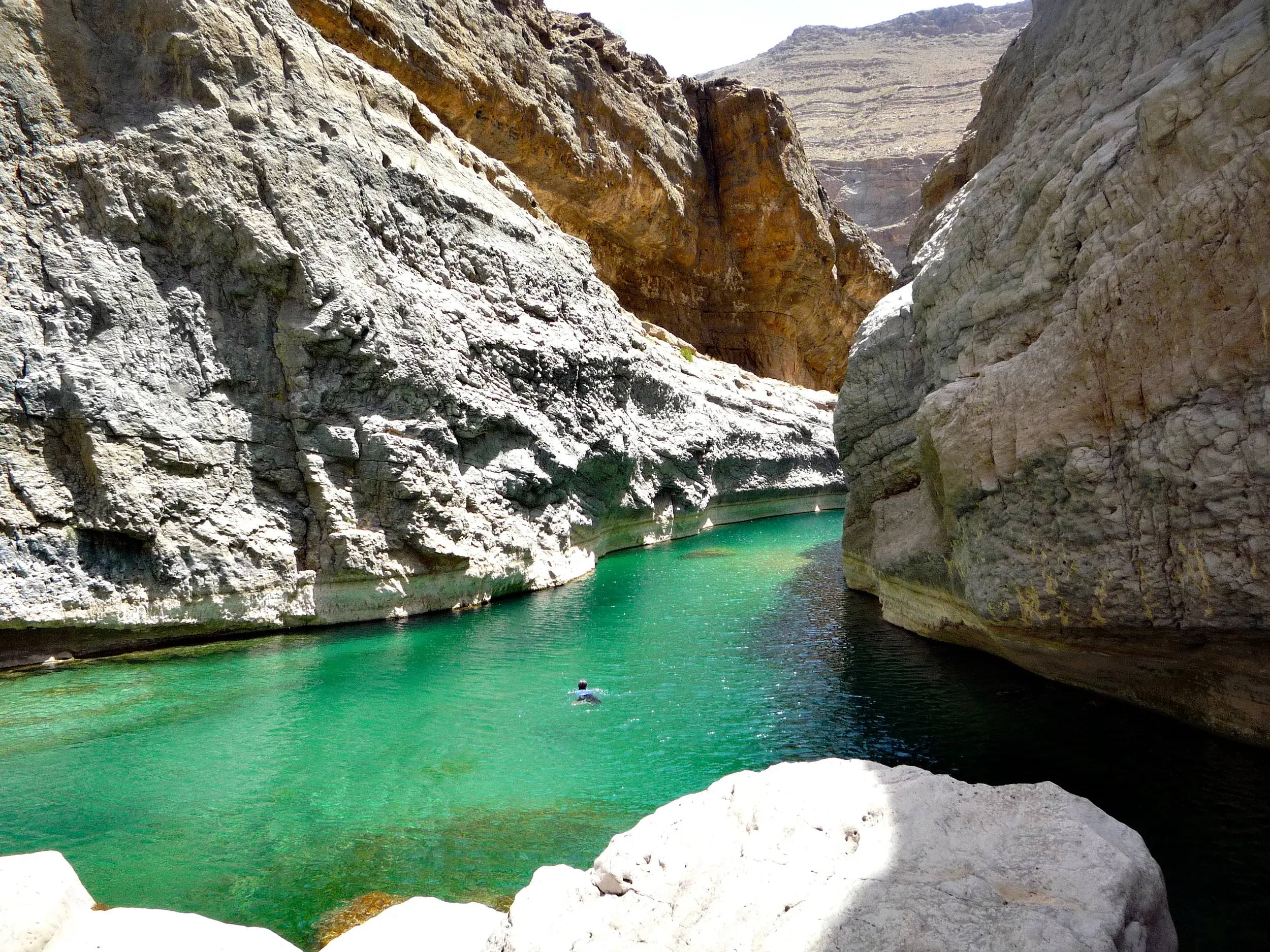 Ein Reisender schwimmt zur Abkühlung durch das türkisgrüne Wasser der engen Felsschlucht im Wadi Shab auf einer Wanderreise im Oman.