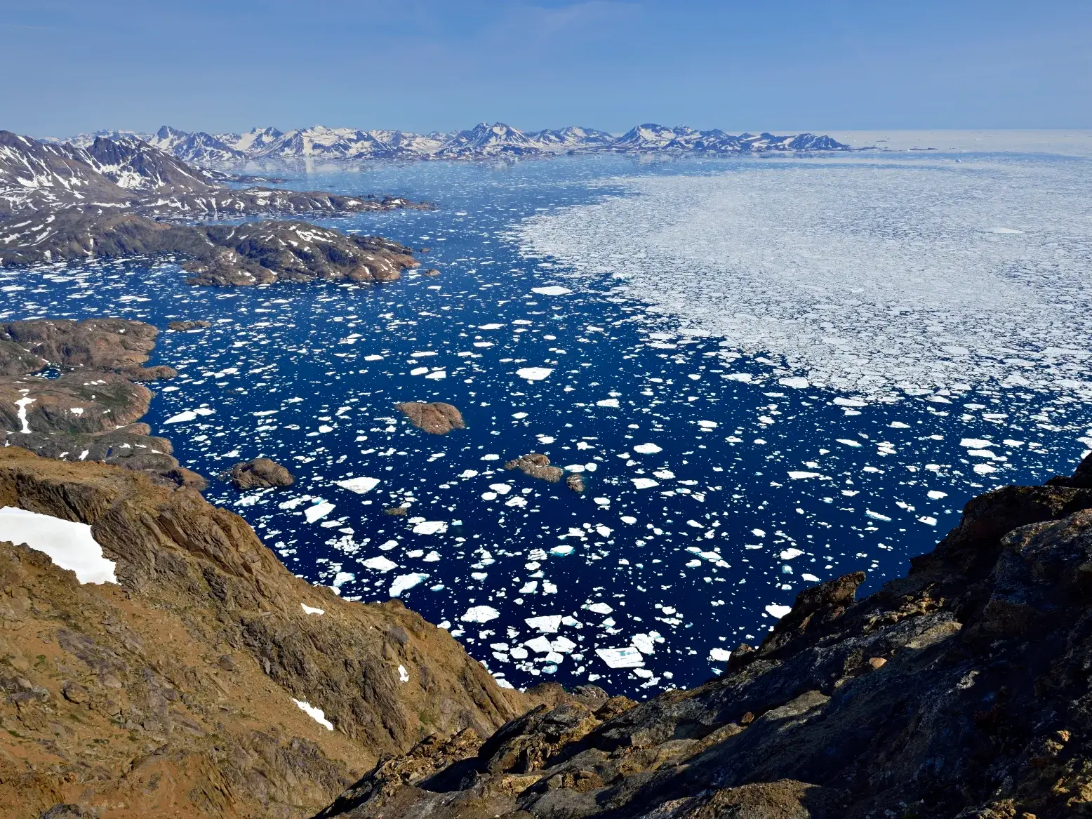 Panoramablick beim Trekking in Ostgrönland: Der eisgefüllte Sermilik-Fjord und schneebedeckte Gipfel am Horizont.