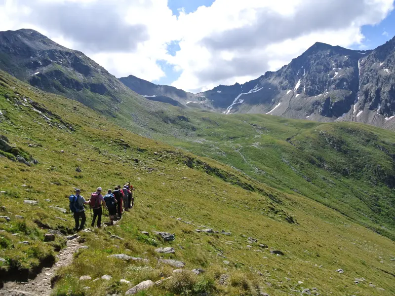 Eine Hauser-Wandergruppe auf einem Trekkingpfad durch grüne Almwiesen im Nationalpark Hohe Tauern in Österreich.