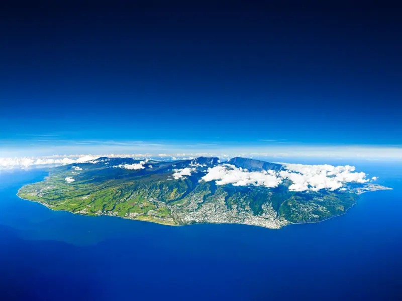Luftaufnahme der gesamten Insel La Réunion, deren grüne Vulkanberge und Talkessel aus dem tiefblauen Indischen Ozean ragen.
