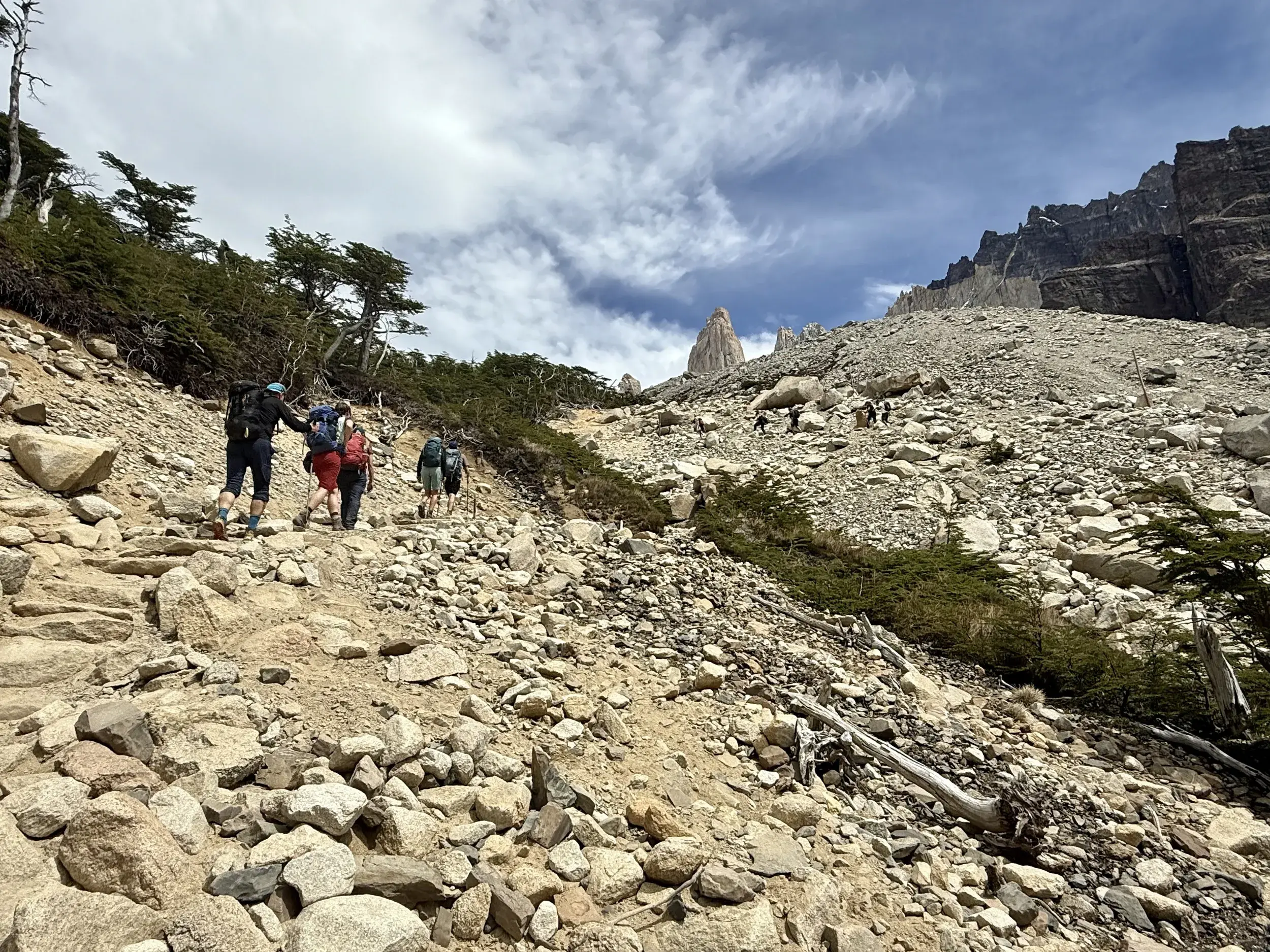Eine Wandergruppe mit Rucksäcken beim anspruchsvollen Aufstieg zu den Torres del Paine über einen steinigen Pfad.