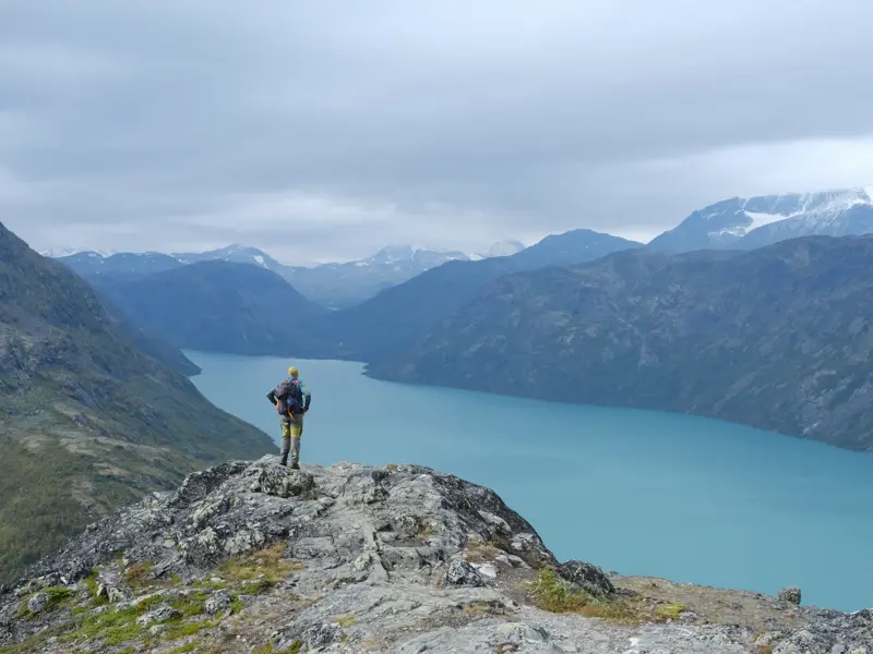 Ein Trekker genießt auf dem Besseggen-Grat die Aussicht auf den türkisen Gjende-See und die Berge von Jotunheimen.