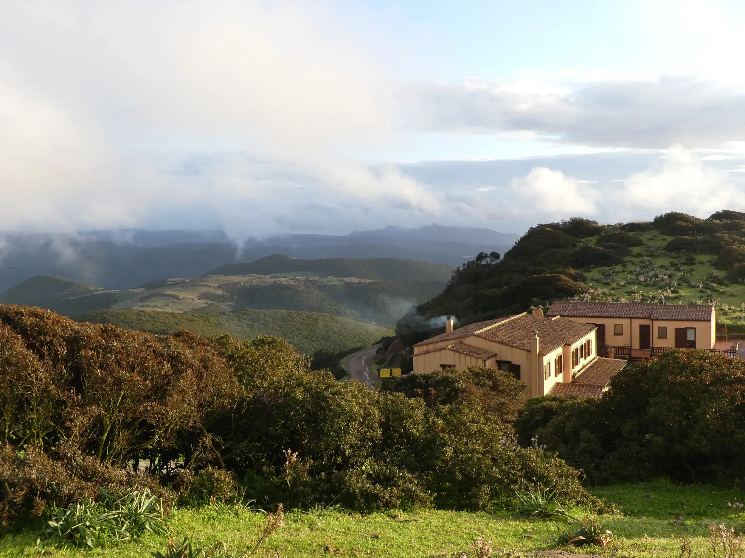 Ein Agriturismo mit Ziegeldach schmiegt sich in die grünen, nebligen Hügel der Berglandschaft Sardiniens am Morgen.