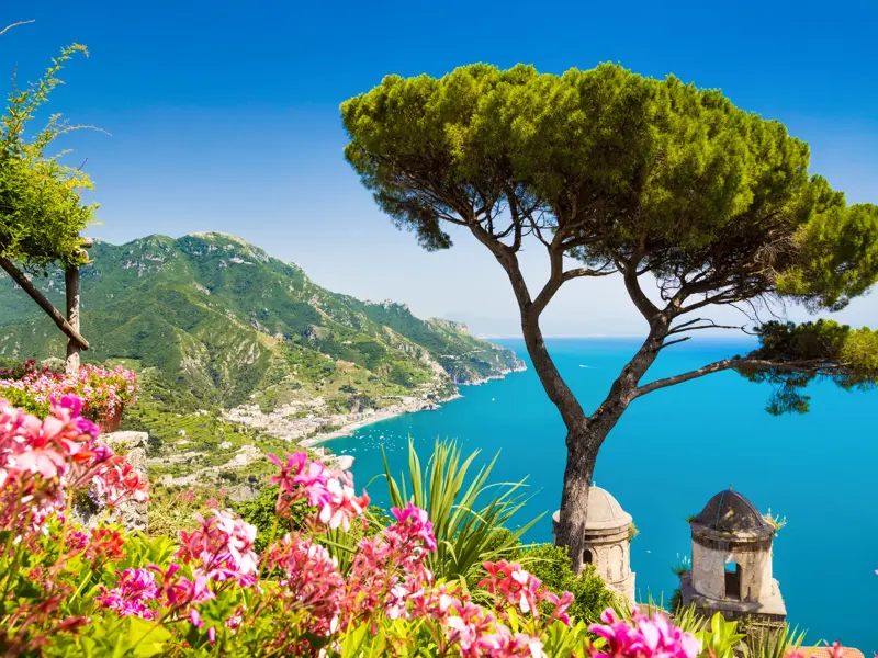 Pinie und Blumen im Garten der Villa Cimbrone in Ravello mit spektakulärem Blick auf die türkisblaue Amalfitana.