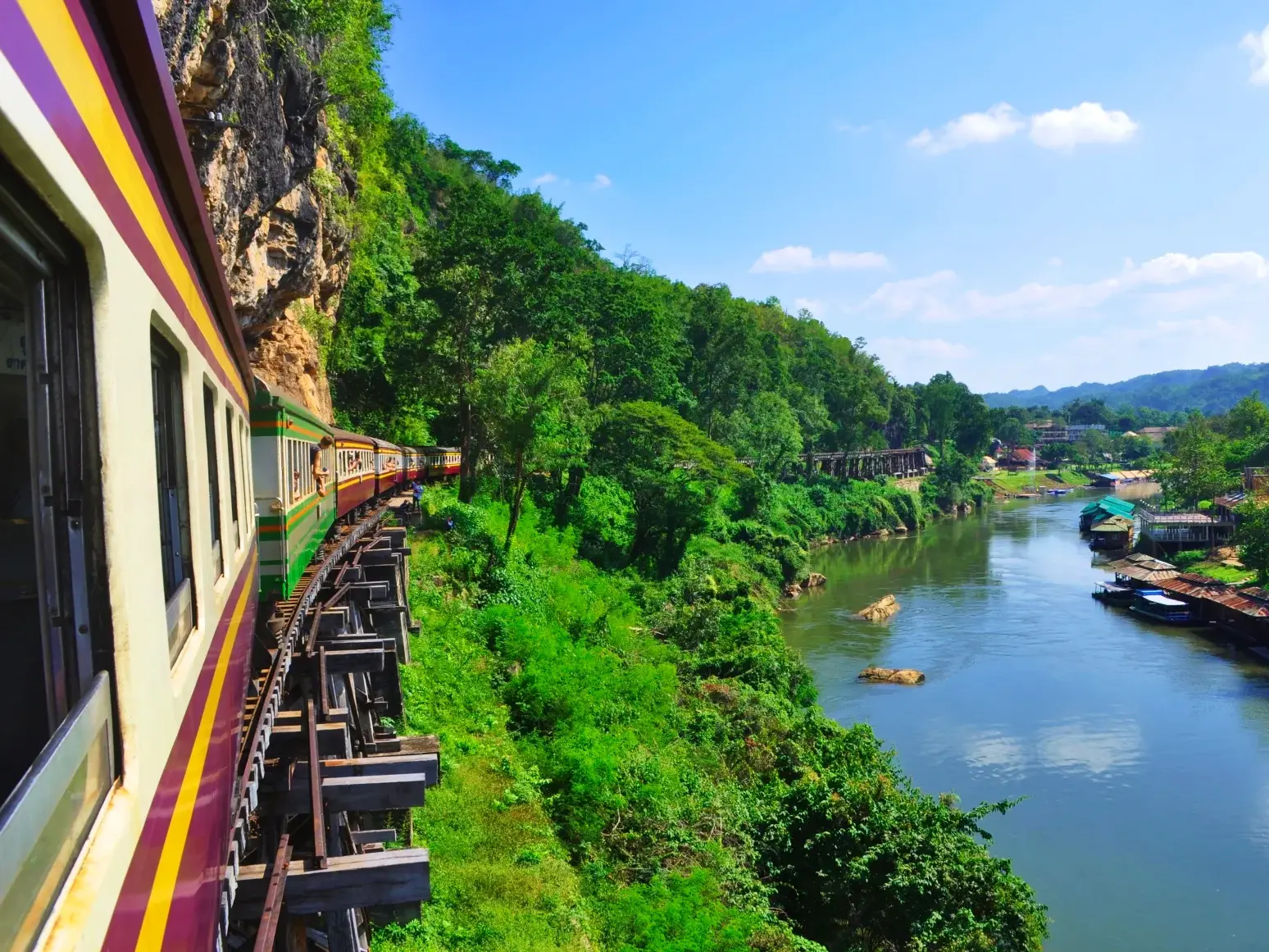 Historischer Zug fährt auf der berühmten Todeseisenbahn-Strecke entlang einer grünen Felswand am River Kwai in Thailand.