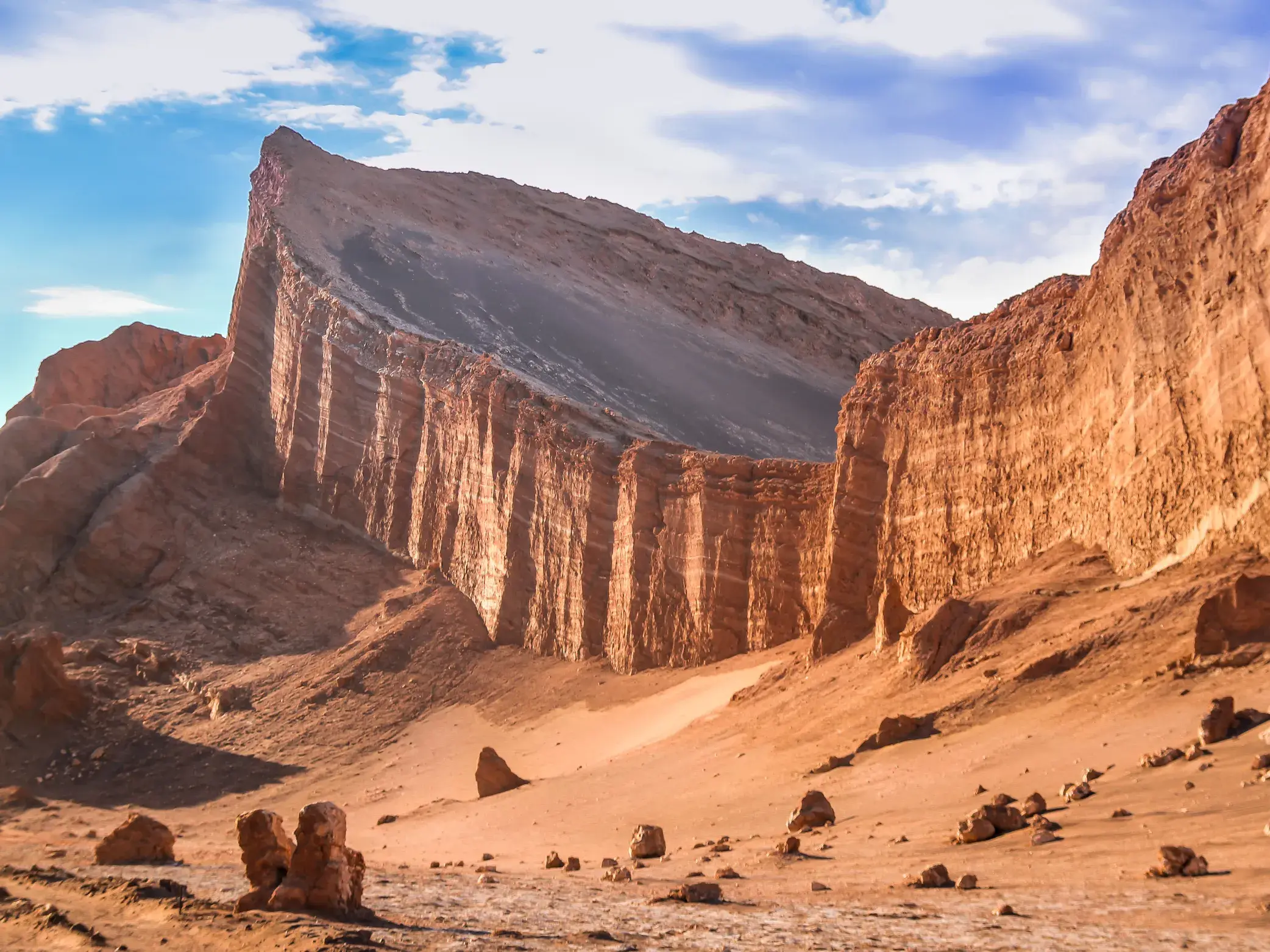 Imposante, rote Felsformation mit steiler Kante in der wüstenhaften Landschaft der Cordillera de la Sal in der Atacama-Wüste.