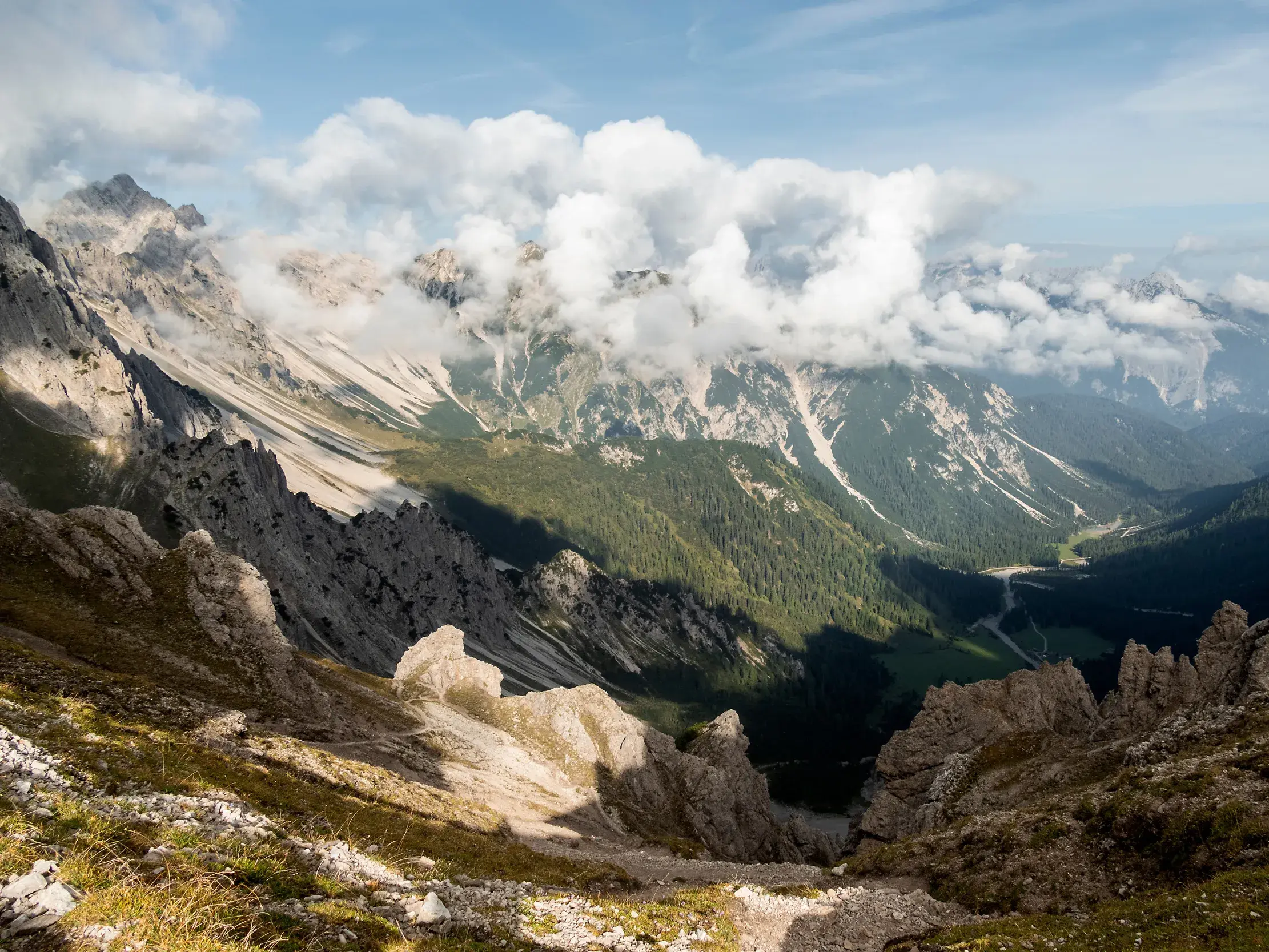 Blick vom Wanderweg über felsige Hänge ins grüne Eppzirler Tal, im Hintergrund die wolkenverhangenen Gipfel des Karwendels.