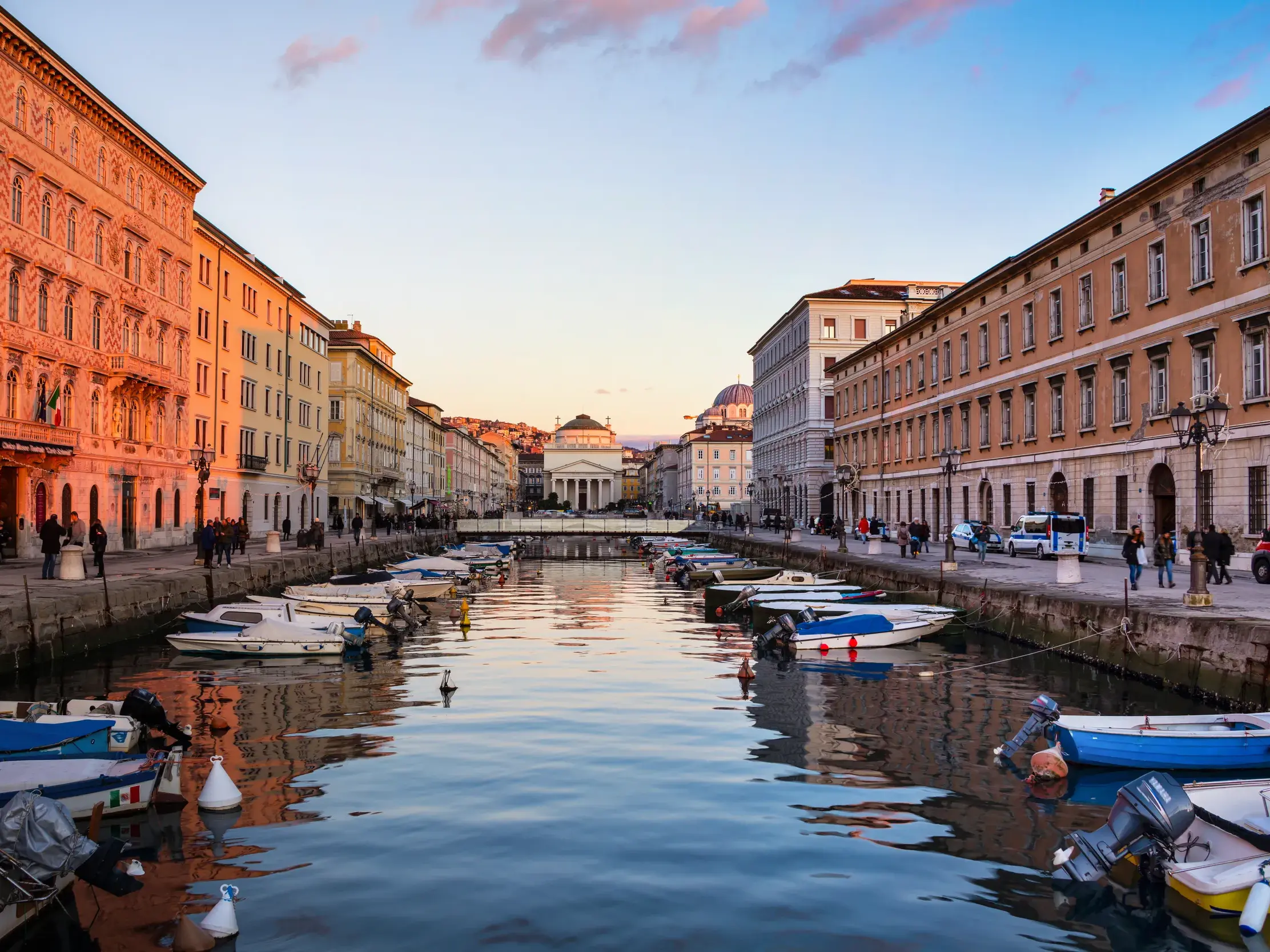 Historische Gebäude und Boote am Canal Grande in Triest im Abendlicht, im Hintergrund die Kirche Sant'Antonio Taumaturgo.