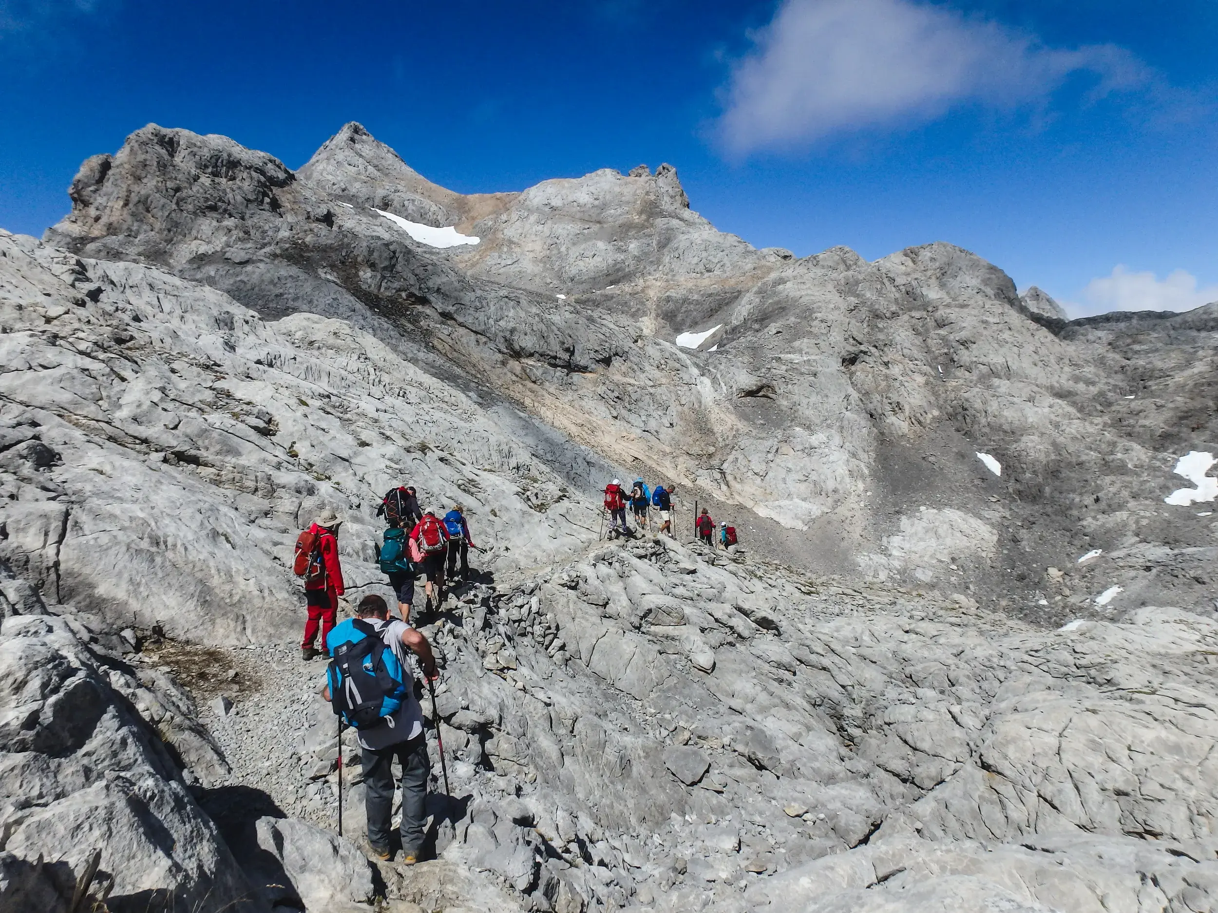 Eine Hauser-Trekkinggruppe wandert auf einem steinigen Bergpfad durch das karge Kalksteinmassiv der Picos de Europa.