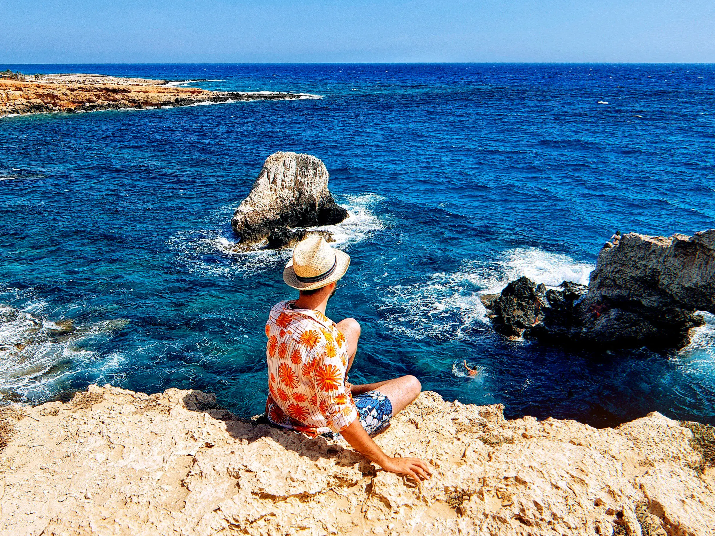 Ein Reisender auf einer Klippe am Aphroditefelsen auf Zypern genießt den Blick über das tiefblaue Mittelmeer bei Paphos.
