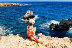 Ein Reisender auf einer Klippe am Aphroditefelsen auf Zypern genießt den Blick über das tiefblaue Mittelmeer bei Paphos.