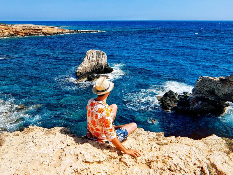 Ein Reisender auf einer Klippe am Aphroditefelsen auf Zypern genießt den Blick über das tiefblaue Mittelmeer bei Paphos.