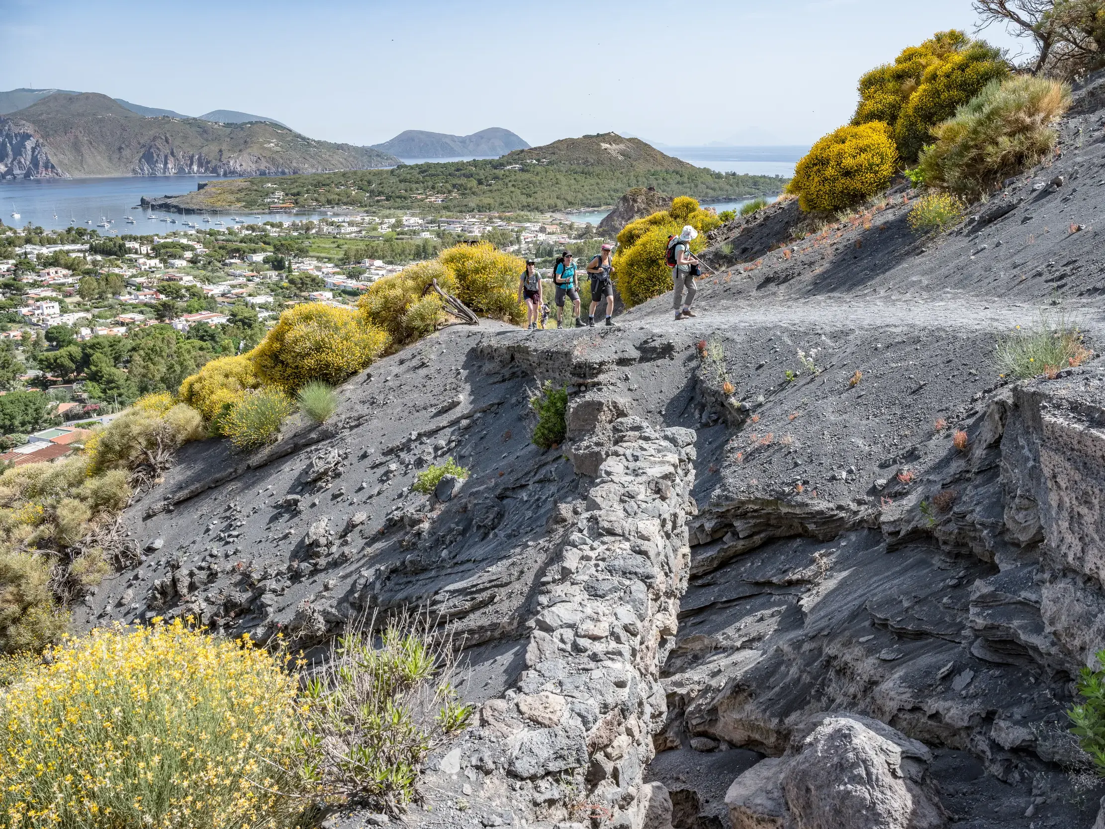 Wandergruppe auf einem Trekkingpfad am Gran Cratere auf Vulcano mit weitem Blick über den Hafen und die Küste der Äolischen Inseln.