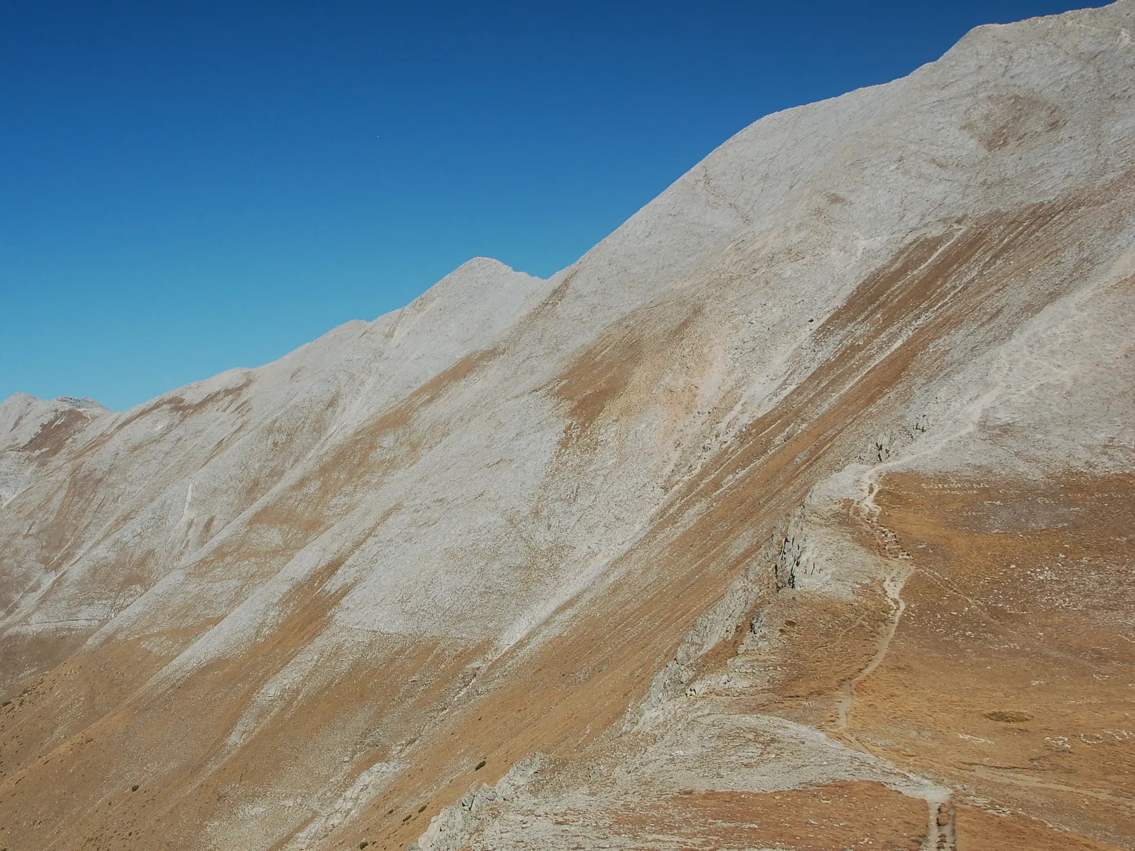Ein schmaler Wanderpfad windet sich am steilen, felsigen Hang des Pirin-Gebirges in Bulgarien unter blauem Himmel.