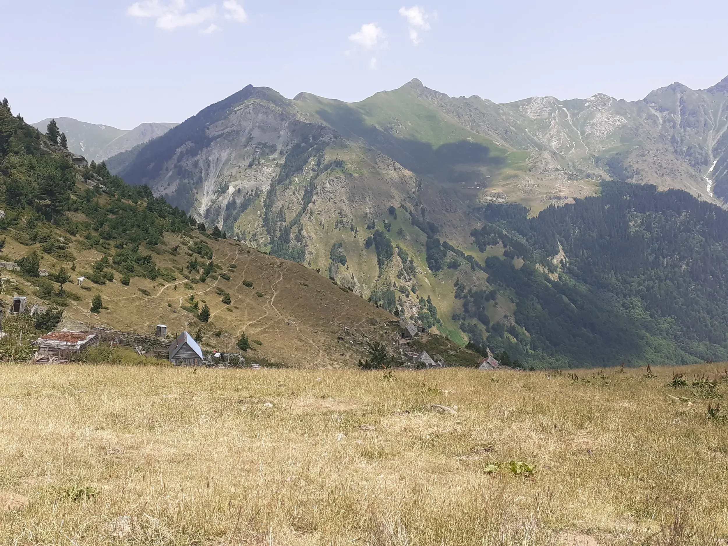 Weite Berglandschaft mit Berghütten im Hochtal von Doberdol während einer Trekkingreise auf dem Peaks of the Balkans Trail.