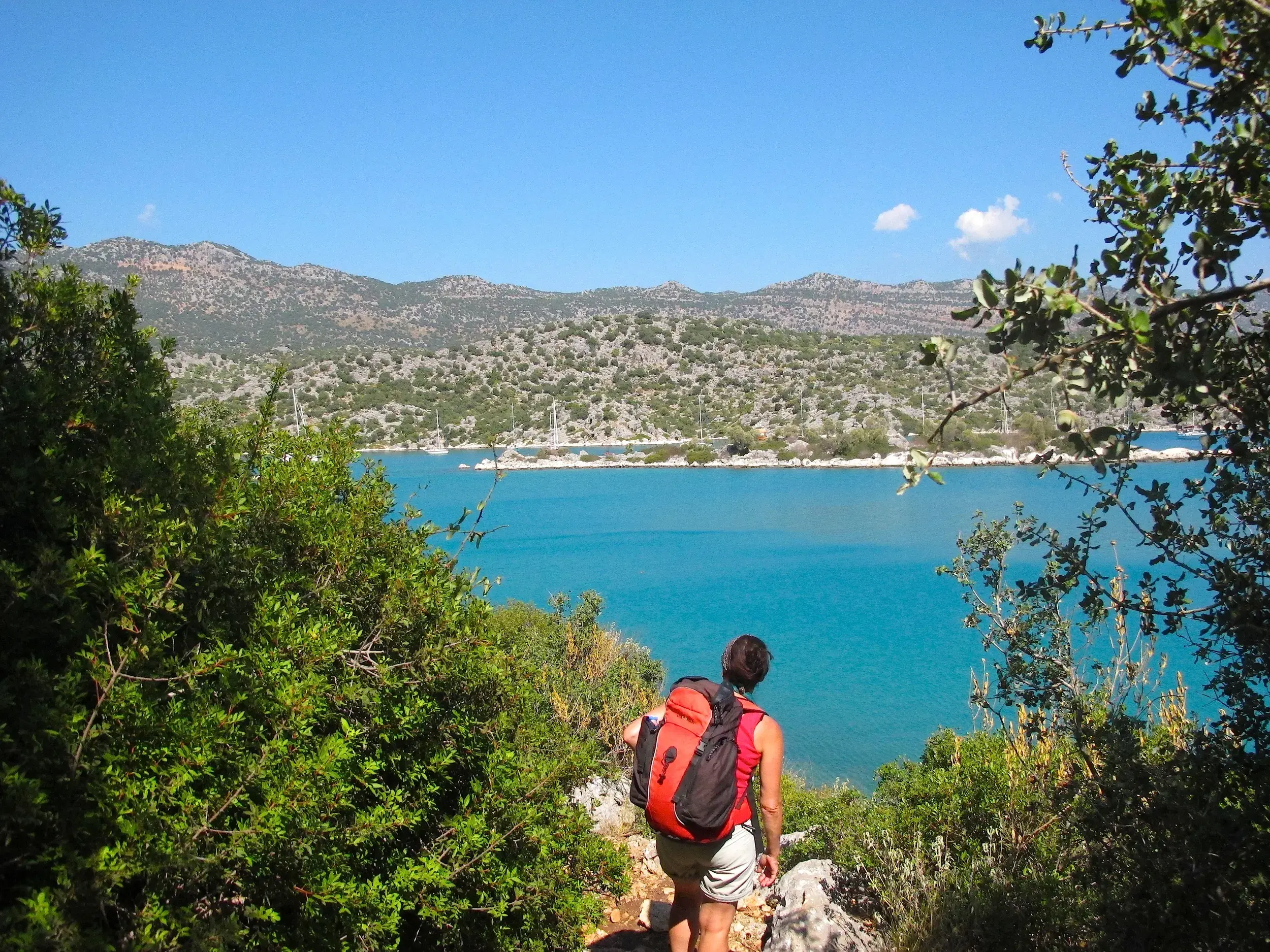 Eine Wanderin mit Rucksack genießt auf dem Lykischen Weg den Ausblick über die türkisfarbene Küste des Mittelmeers.