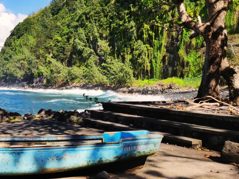 Altes, blaues Fischerboot an der wildromantischen Vulkanküste von La Réunion mit üppig grünen Klippen und rauer Brandung.
