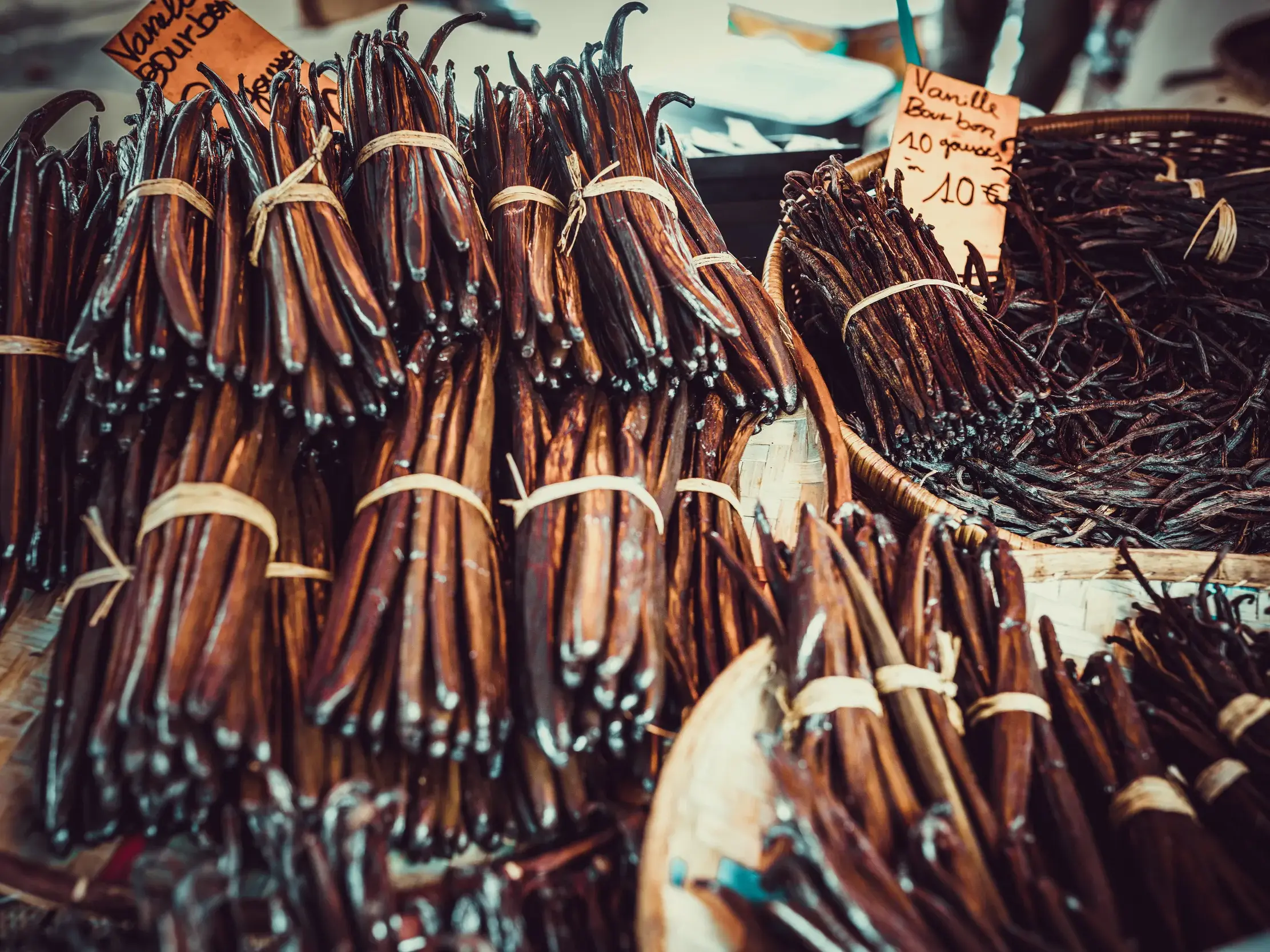 Zahlreiche Bündel frischer Bourbon-Vanilleschoten in Weidenkörben mit Preisschildern auf einem Markt auf La Réunion.