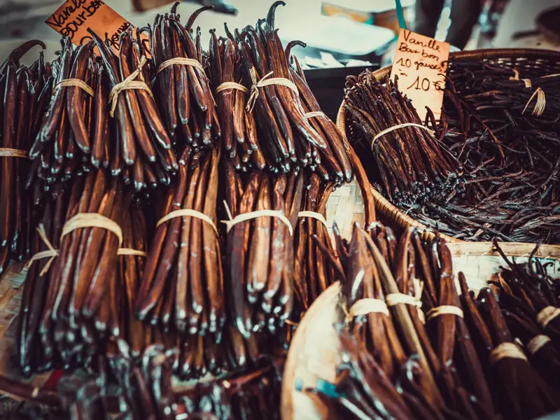 Zahlreiche Bündel frischer Bourbon-Vanilleschoten in Weidenkörben mit Preisschildern auf einem Markt auf La Réunion.