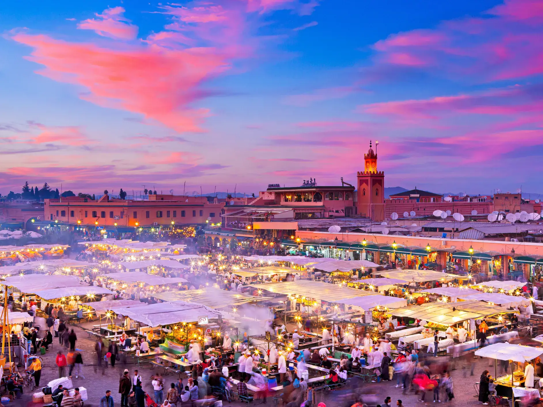 Pulsierender Marktplatz Djemaa el-Fna in Marrakesch bei Sonnenuntergang mit Menschenmengen an beleuchteten Garküchen.