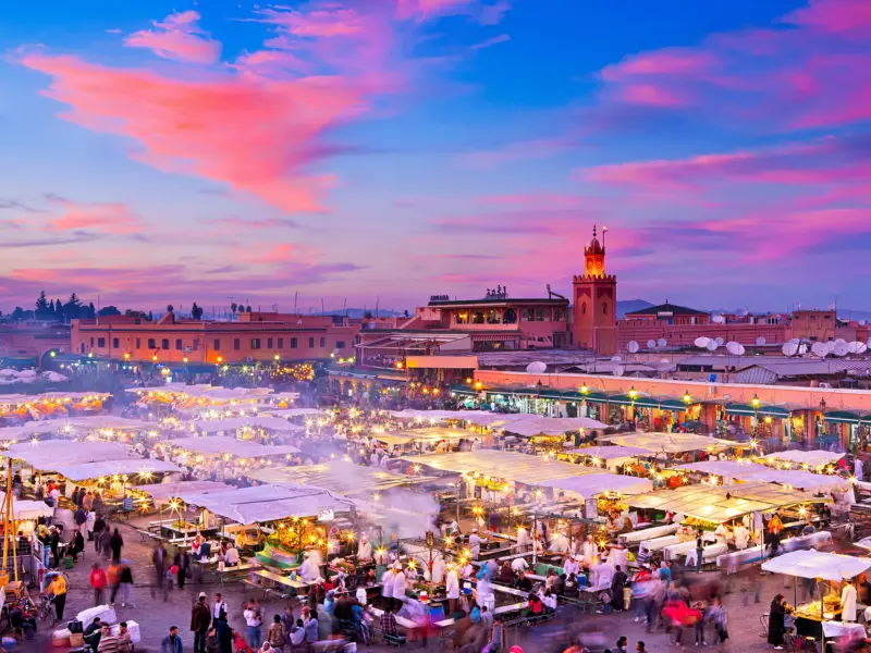 Pulsierender Marktplatz Djemaa el-Fna in Marrakesch bei Sonnenuntergang mit Menschenmengen an beleuchteten Garküchen.
