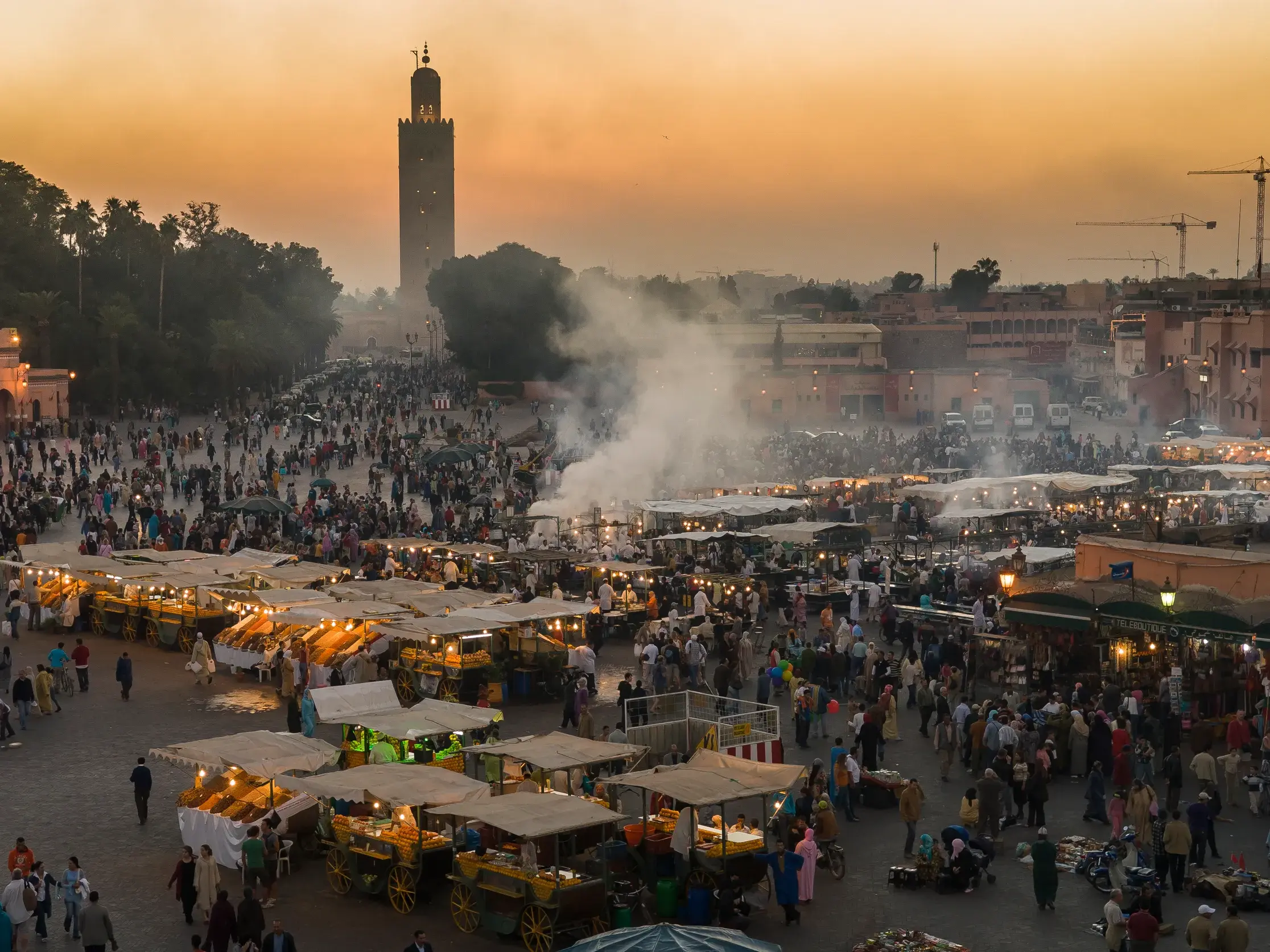 Abendstimmung auf dem belebten Djemaa el Fna in Marrakesch mit Garküchen, Menschenmassen und der Koutoubia-Moschee.