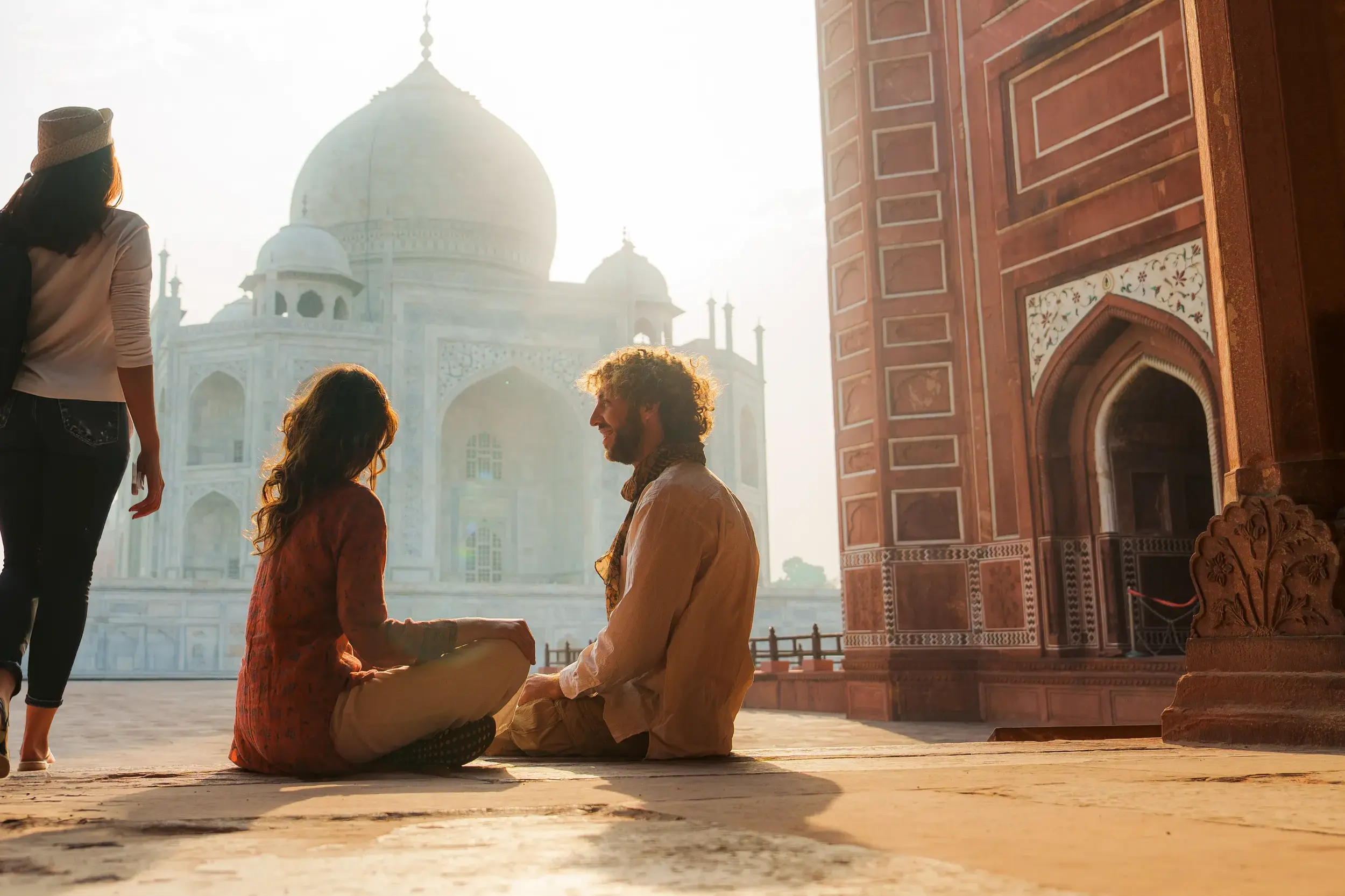 Junge Reisende entspannen im warmen Morgenlicht auf dem Vorplatz des berühmten Taj Mahal Mausoleums in Agra, Indien.