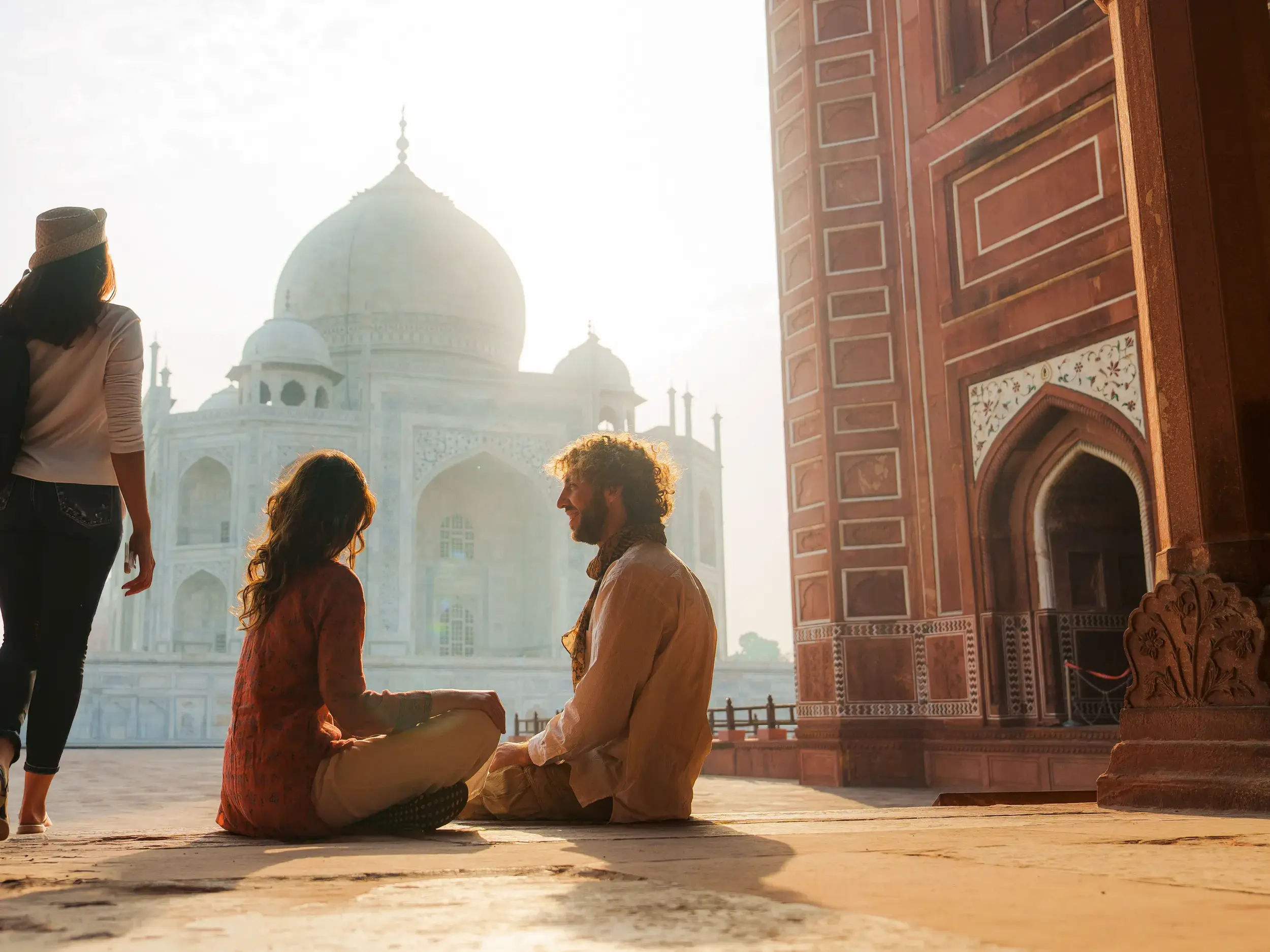 Junge Reisende entspannen im warmen Morgenlicht auf dem Vorplatz des berühmten Taj Mahal Mausoleums in Agra, Indien.