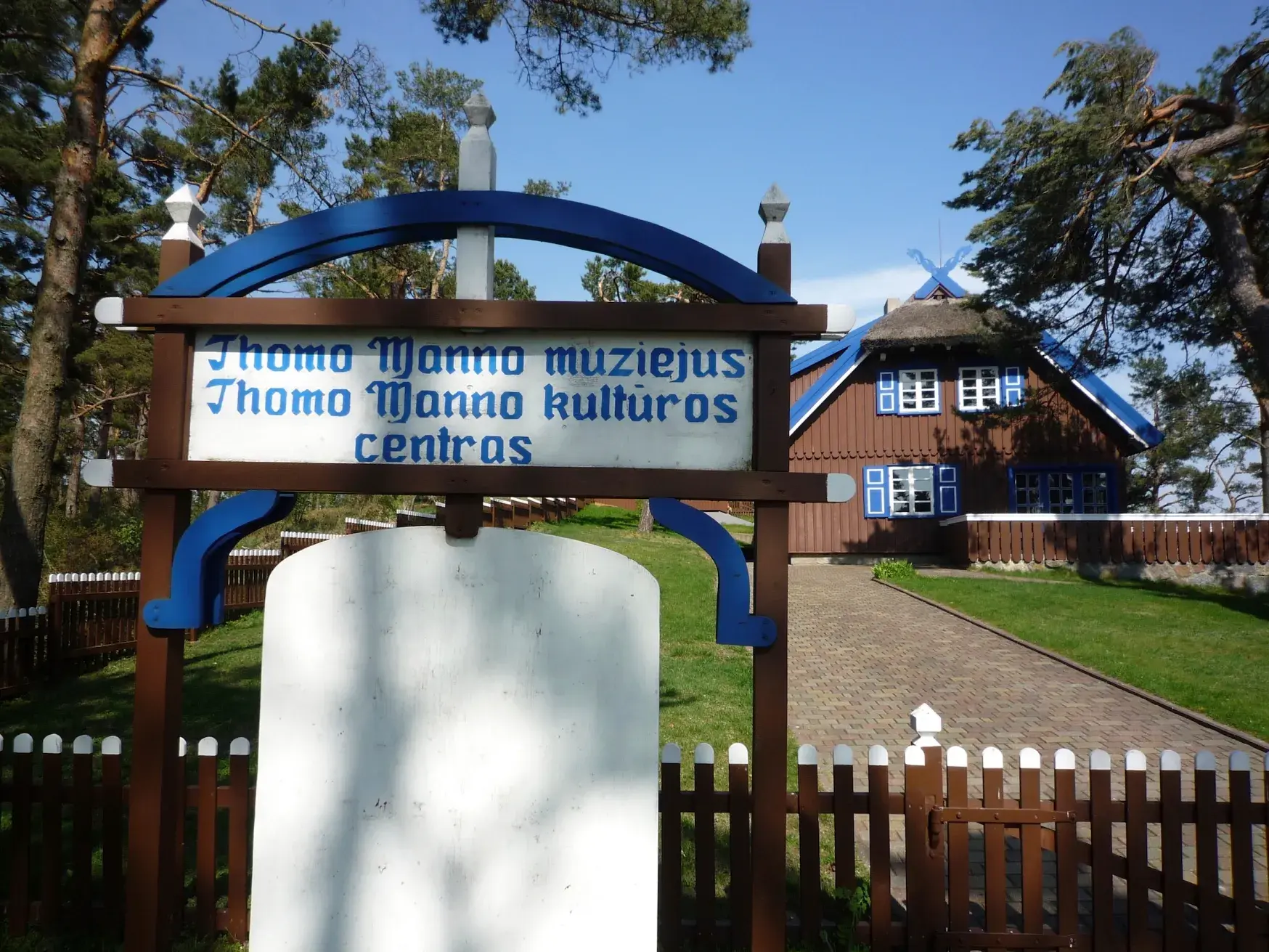 Holzschild des Thomas-Mann-Museums in Nida, im Hintergrund das traditionelle Sommerhaus auf der Kurischen Nehrung.
