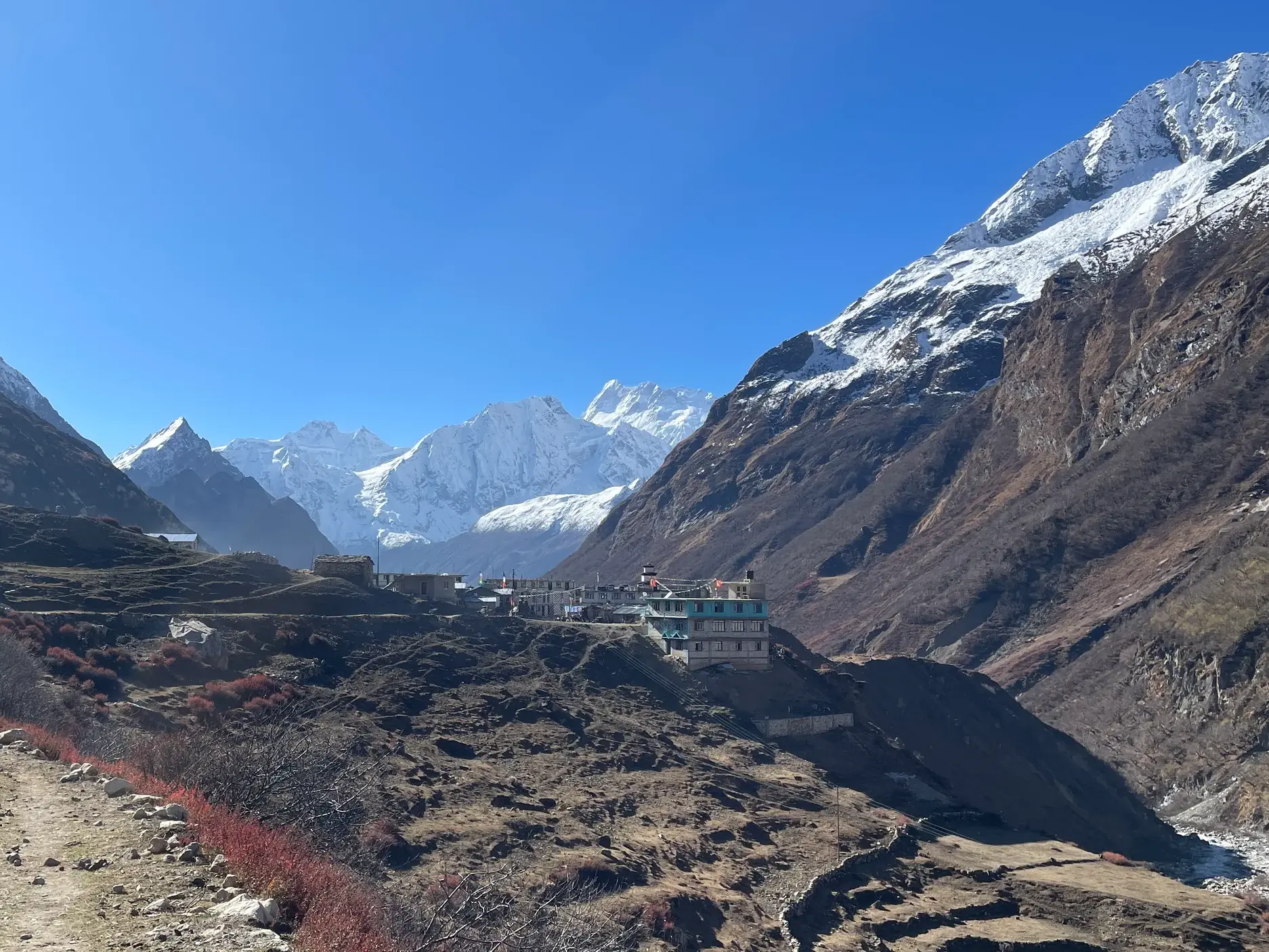 Blick auf das Bergdorf Sama Gaon während des Manaslu Circuit Trekkings vor schneebedeckten Himalaya-Gipfeln in Nepal.