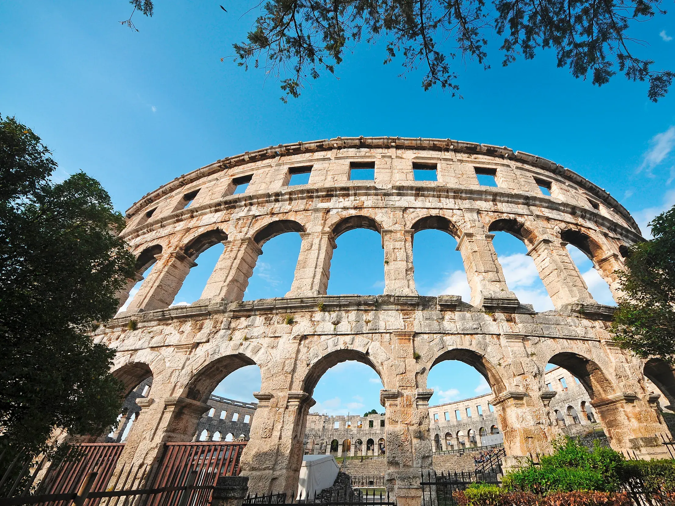 Froschperspektive auf die monumentale Fassade des antiken Amphitheaters in Pula, Istrien, bei strahlend blauem Himmel.