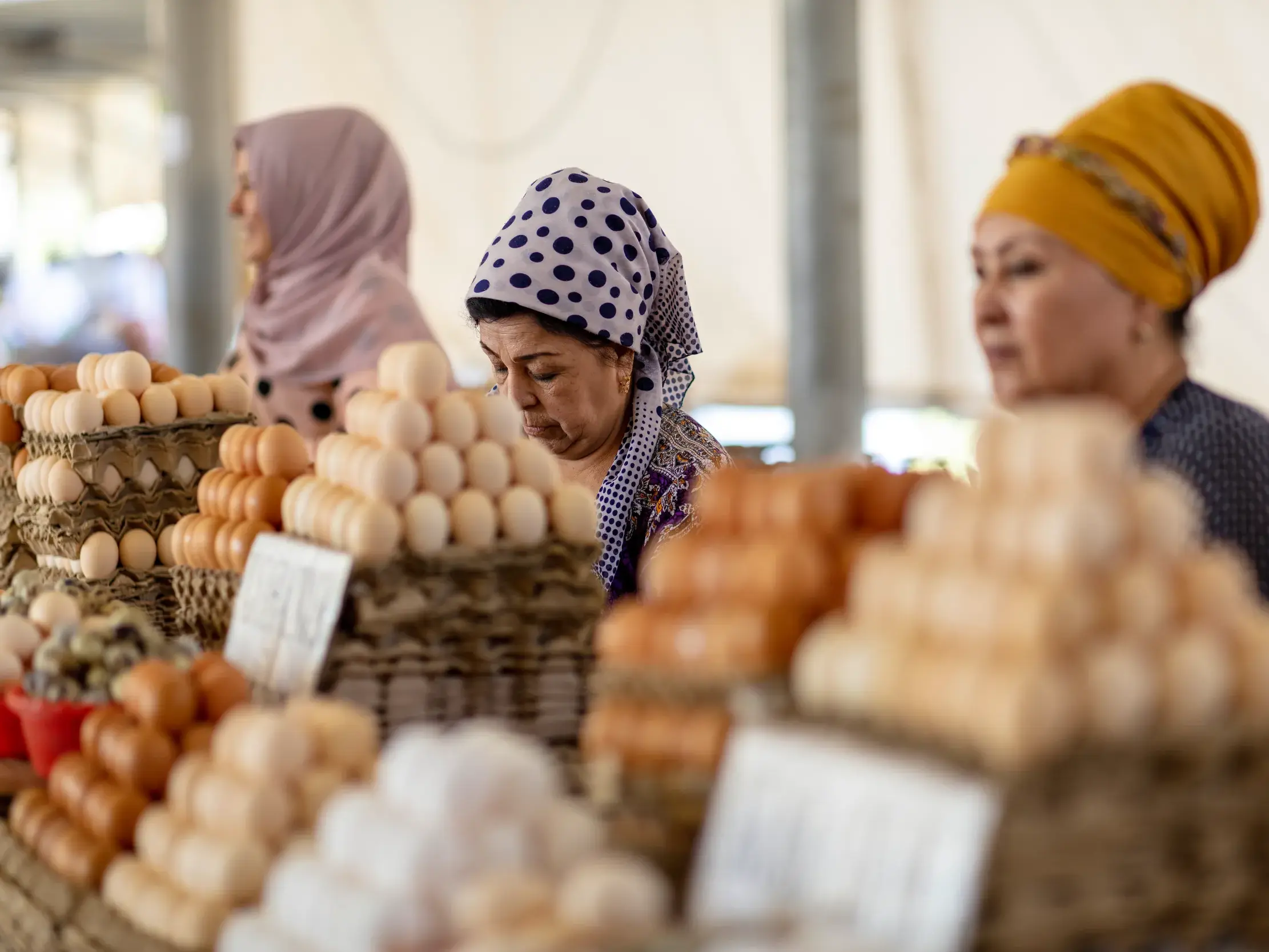 Drei Händlerinnen mit traditionellen Kopftüchern verkaufen auf einem Basar in Samarkand sorgfältig gestapelte Eier.