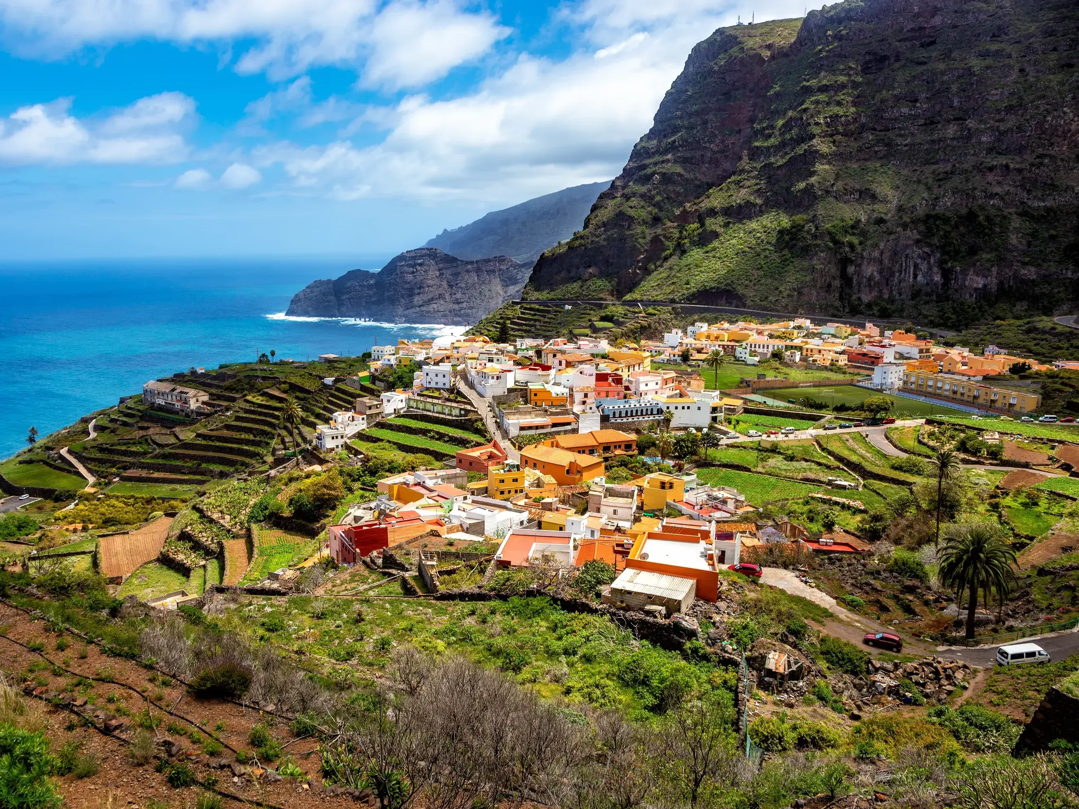 Malerisches Dorf Agulo auf La Gomera mit bunten Häusern, umgeben von grünen Terrassenfeldern an der Steilküste des Atlantiks.