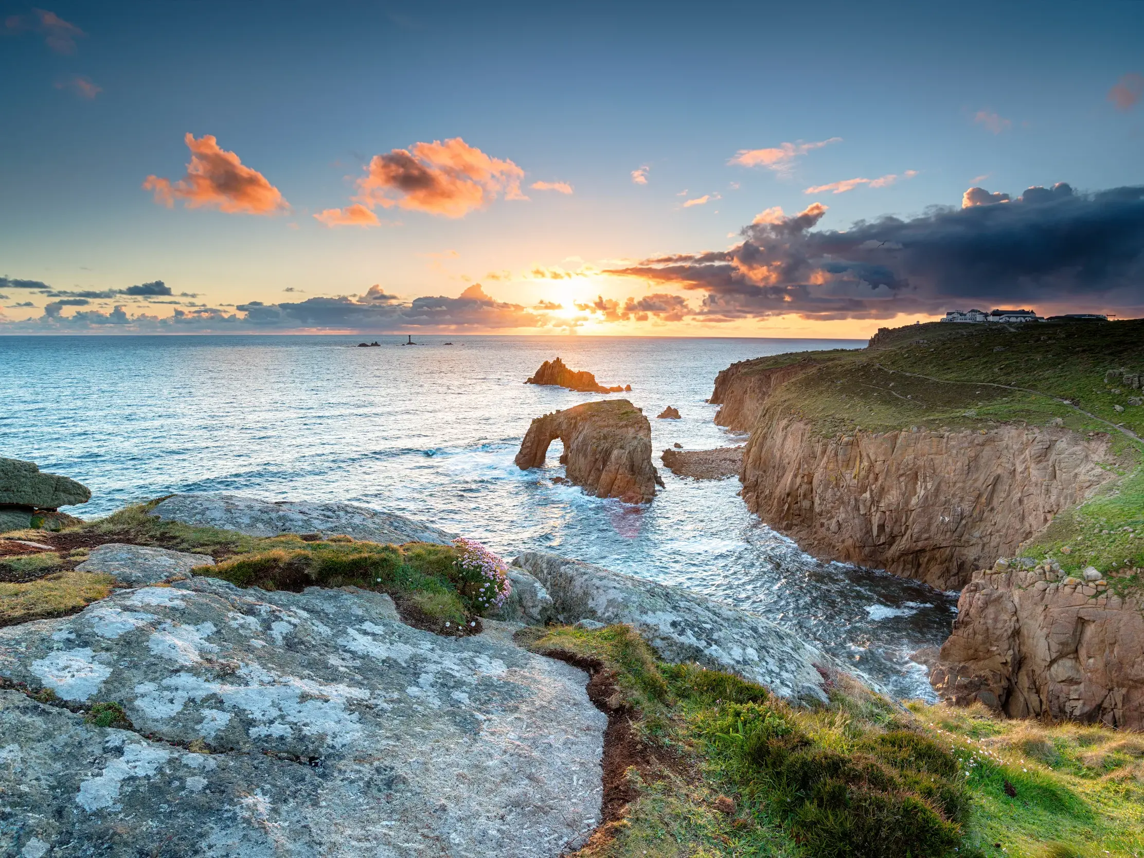 Abendstimmung beim Trekking an der Küste von Cornwall: Die Sonne geht hinter dem Felsentor bei Land's End unter.