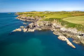 Sonnige Luftaufnahme der zerklüfteten Felsenküste am Pembrokeshire Coast Path mit grünen Wiesen und türkisblauem Meer in Wales.