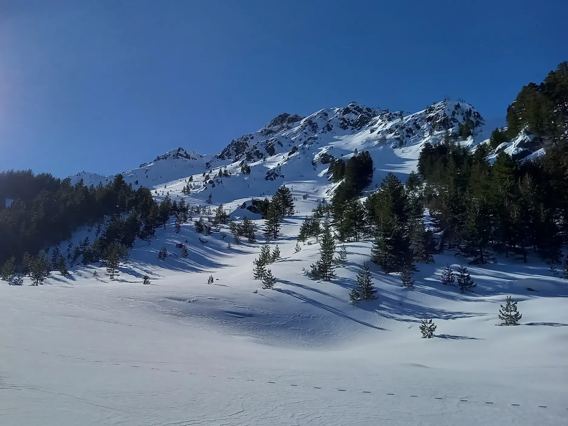 Zwei Personen auf Skitour durchqueren eine weite, unberührte Schneelandschaft im sonnigen Sharr-Gebirge im Kosovo.