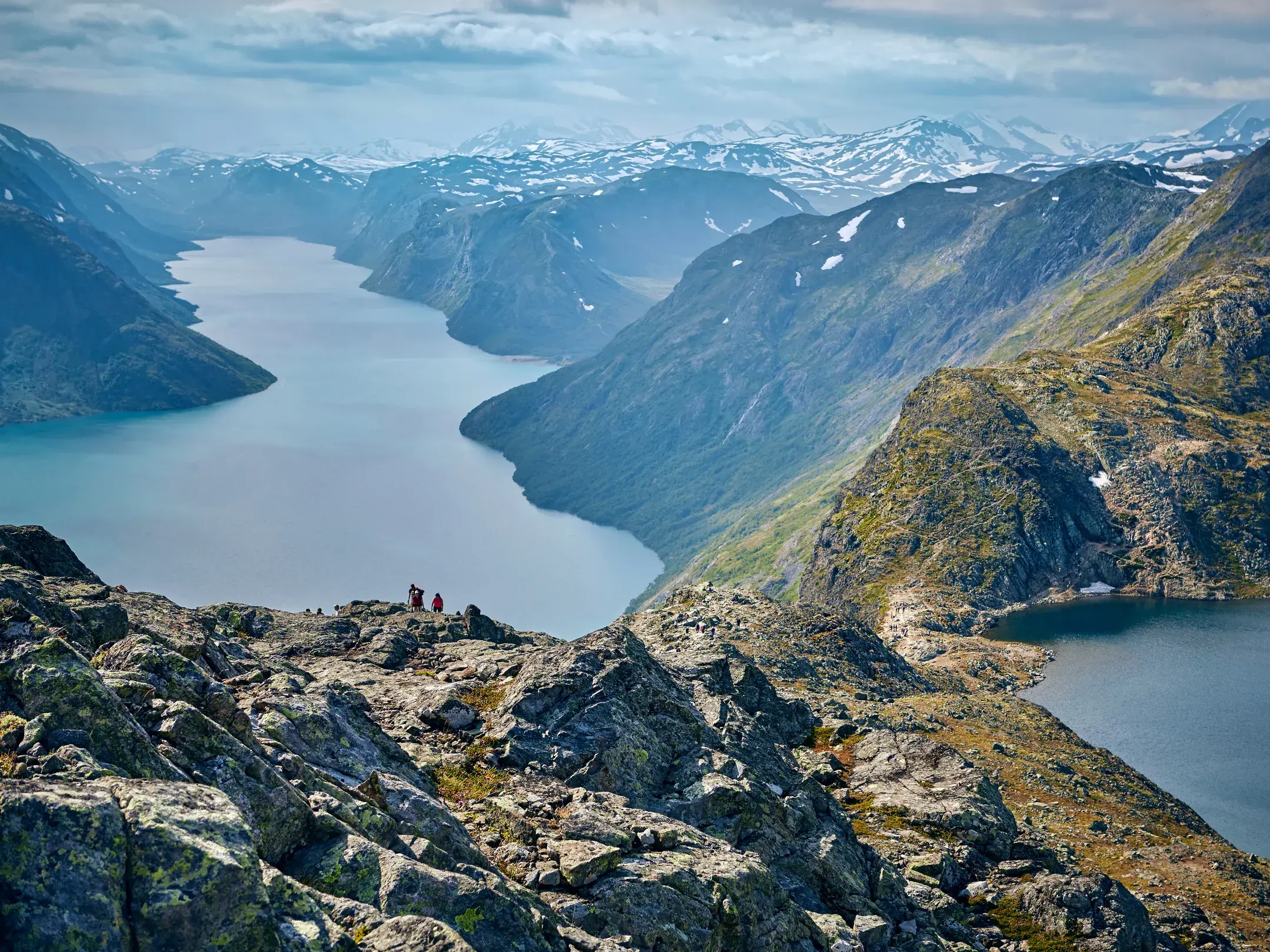 Zwei Wanderer auf dem felsigen Besseggen-Grat mit Blick auf den türkisen Gjende-See und das weite Bergpanorama Jotunheimens.