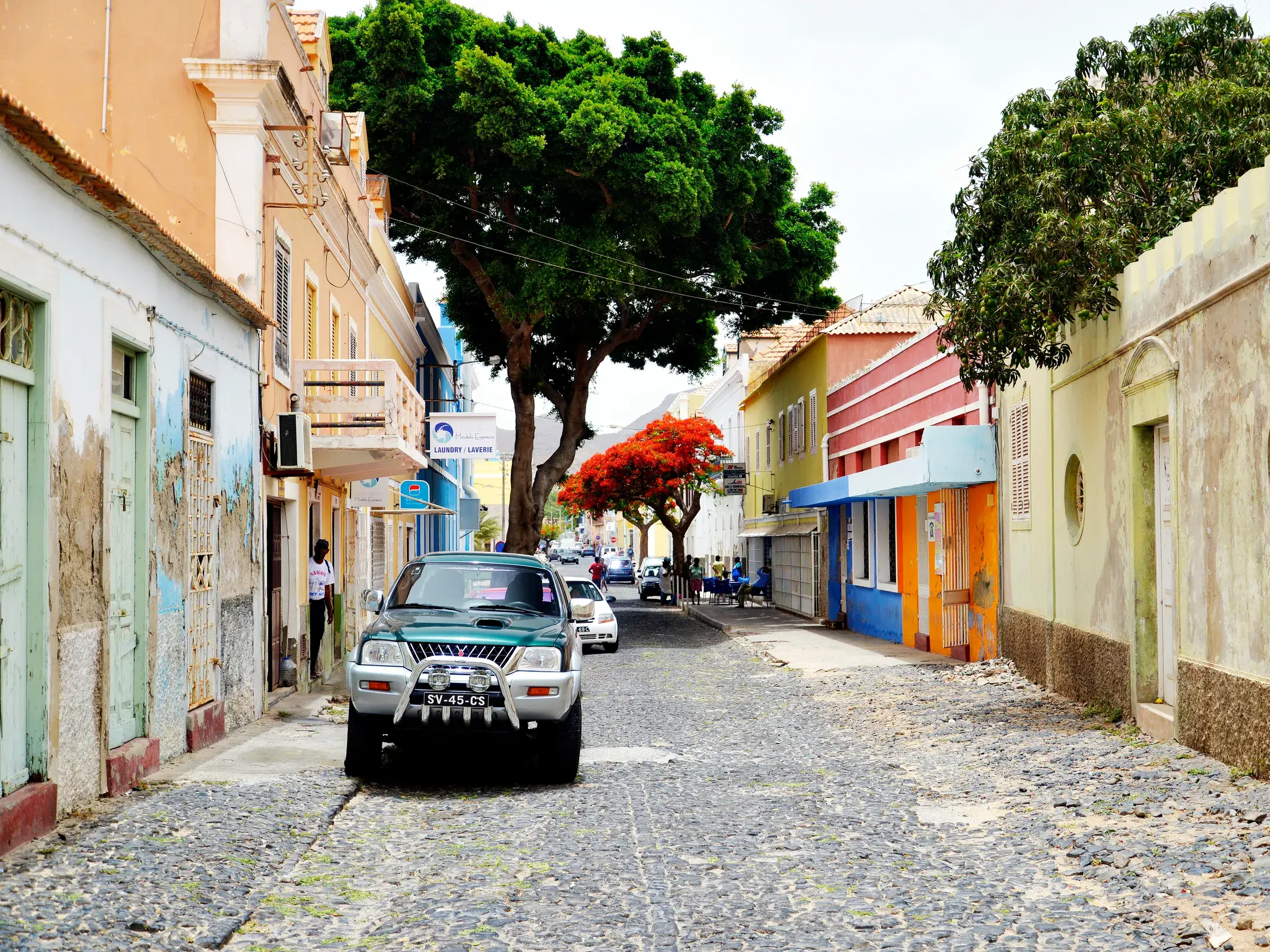 Ein Geländewagen fährt durch eine Gasse mit Kopfsteinpflaster in Mindelo, gesäumt von bunten Kolonialbauten auf São Vicente.