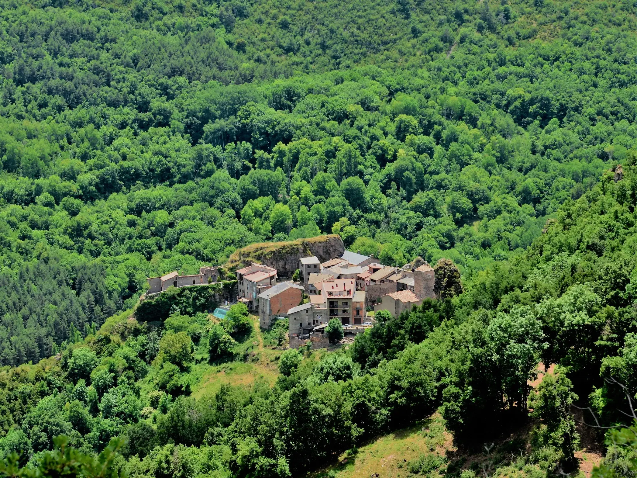 Abgelegenes, historisches Bergdorf mit Steinhäusern in den südlichen Pyrenäen, umgeben von dichten, sattgrünen Wäldern.