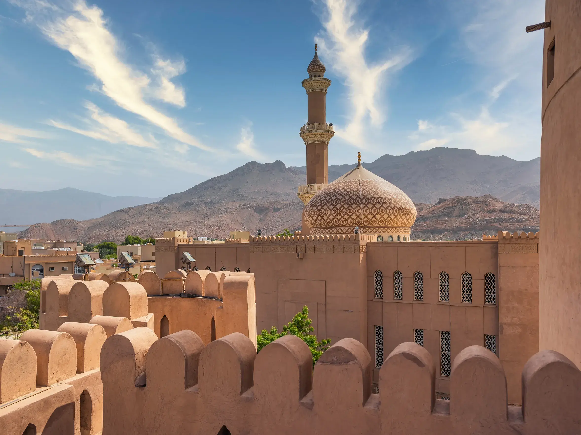 Blick über die Zinnen der Festung von Nizwa auf die Moschee mit goldener Kuppel vor der Kulisse des Hadschargebirges.