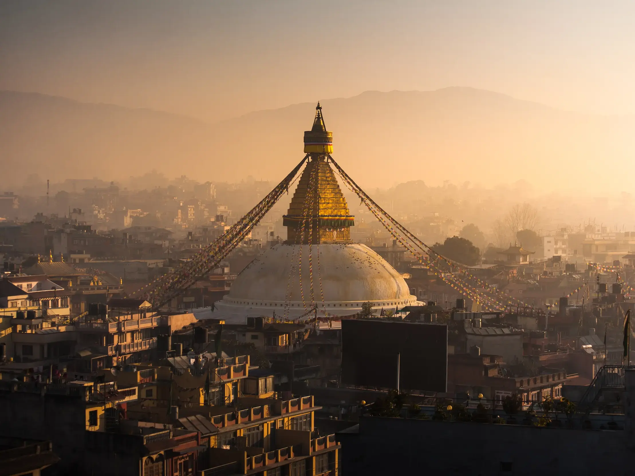 Die beeindruckende Bodnath-Stupa in Kathmandu, von der Gebetsfahnen ausgehen, im goldenen Sonnenaufgang über der Stadt.