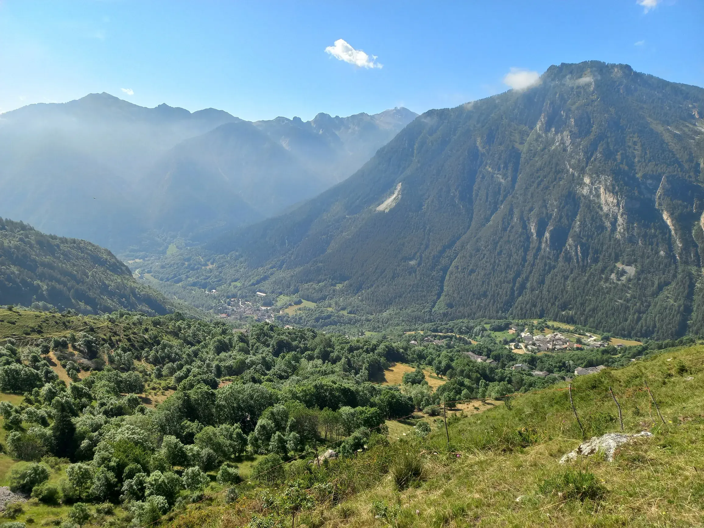 Panoramablick von einem Wanderweg über das grüne Maira-Tal mit kleinen Dörfern und bewaldeten Berghängen im Piemont.